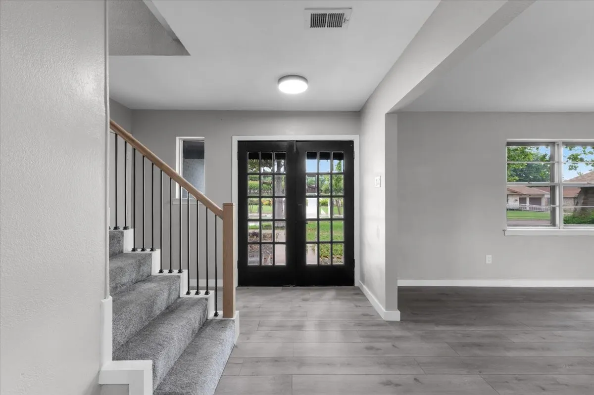 Entryway featuring a black multi-pane door, light gray walls, wood-finish flooring, and a carpeted staircase with wood handrails and black metal balusters