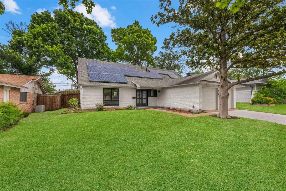 White stucco exterior featuring a dark entry door, multiple solar panels on the roof, and an attached two-car garage