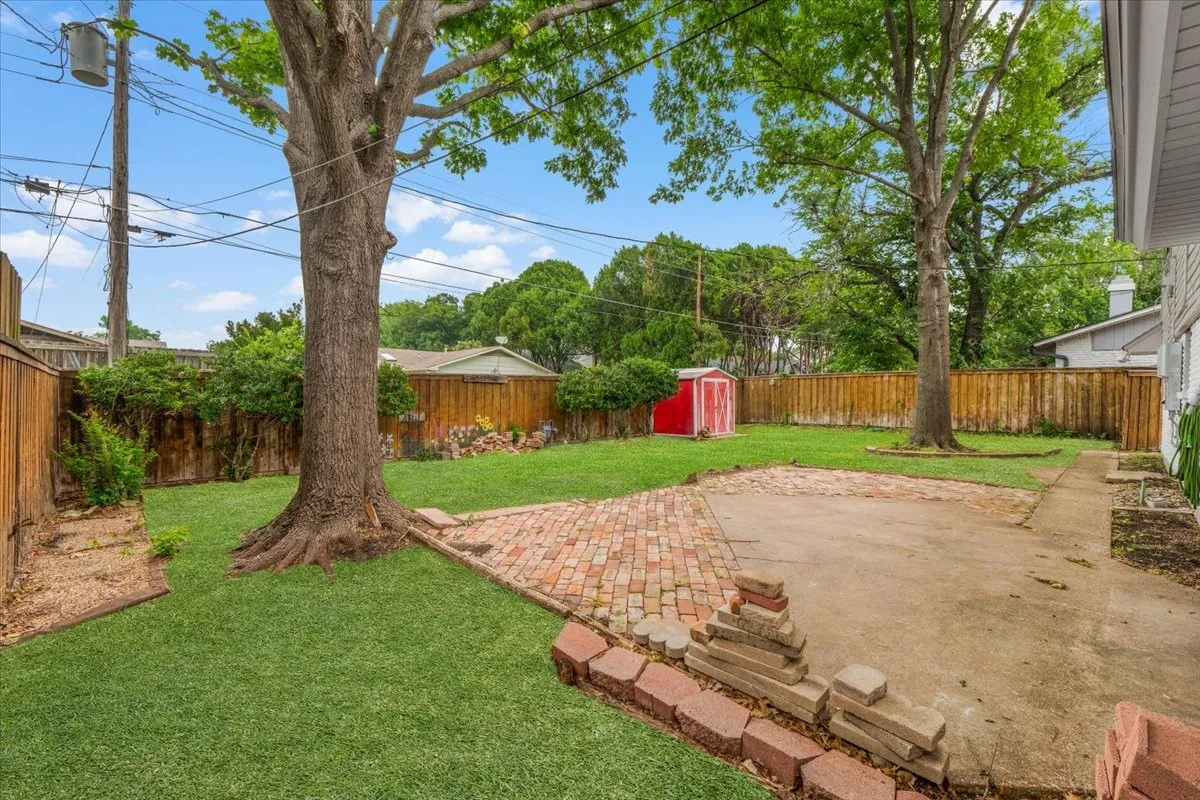 Spacious backyard featuring a manicured lawn, established shade trees, a brick paver patio, a concrete patio area, and wood privacy fencing