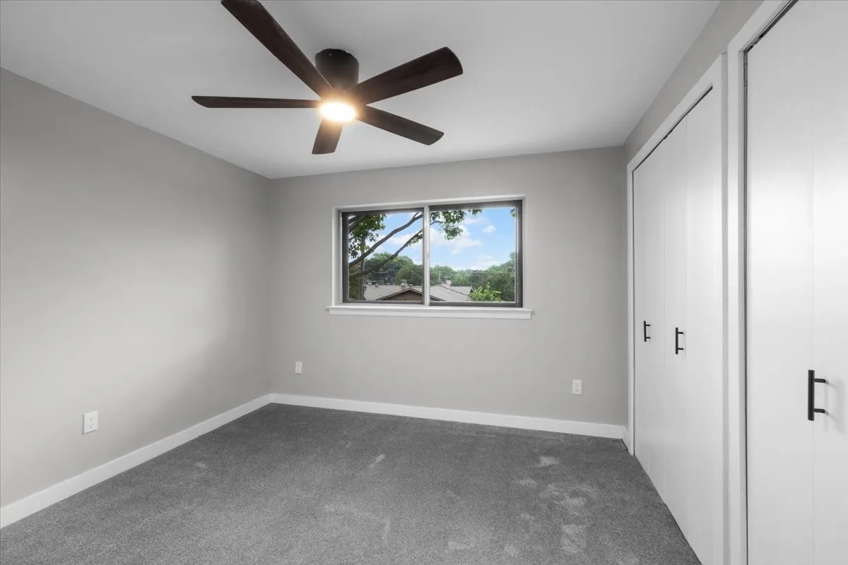 Neutral-toned room featuring a single window with dark trim, a ceiling fan with integrated lighting, and two closet doors with matte black hardware