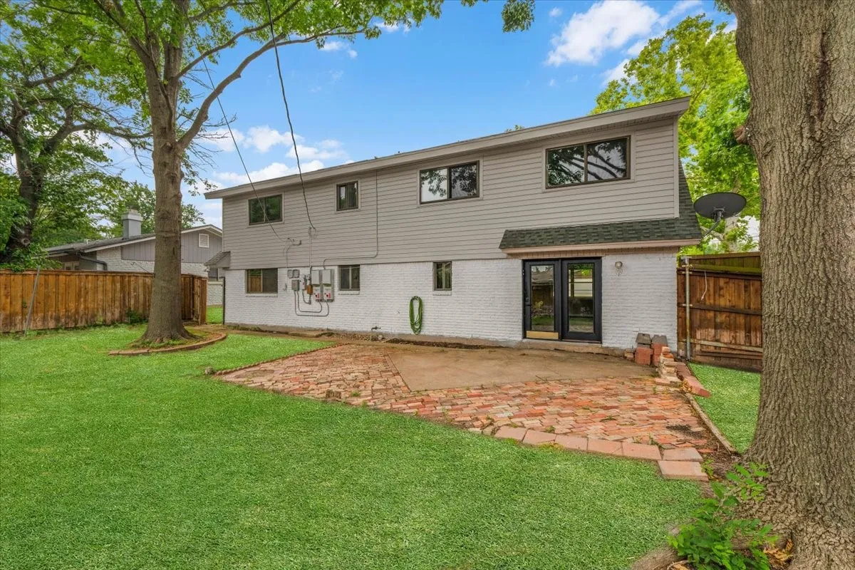 Expansive backyard featuring a manicured lawn, a brick patio, and mature trees