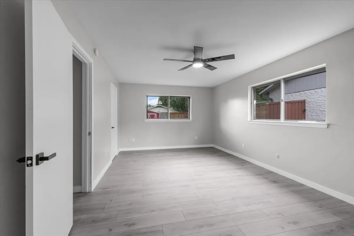 Spacious room featuring light gray walls, wood-finish flooring, and multiple windows