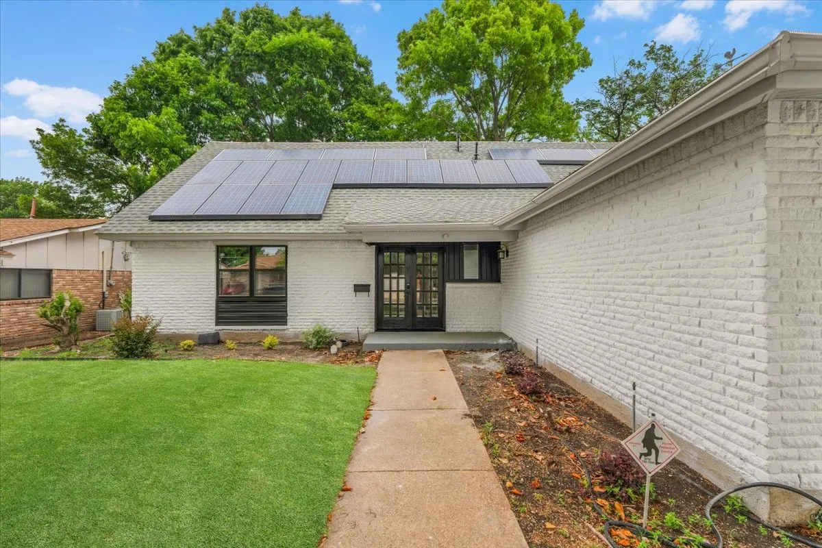 White painted brick exterior featuring solar panels, a dark-framed window, and a segmented glass front door