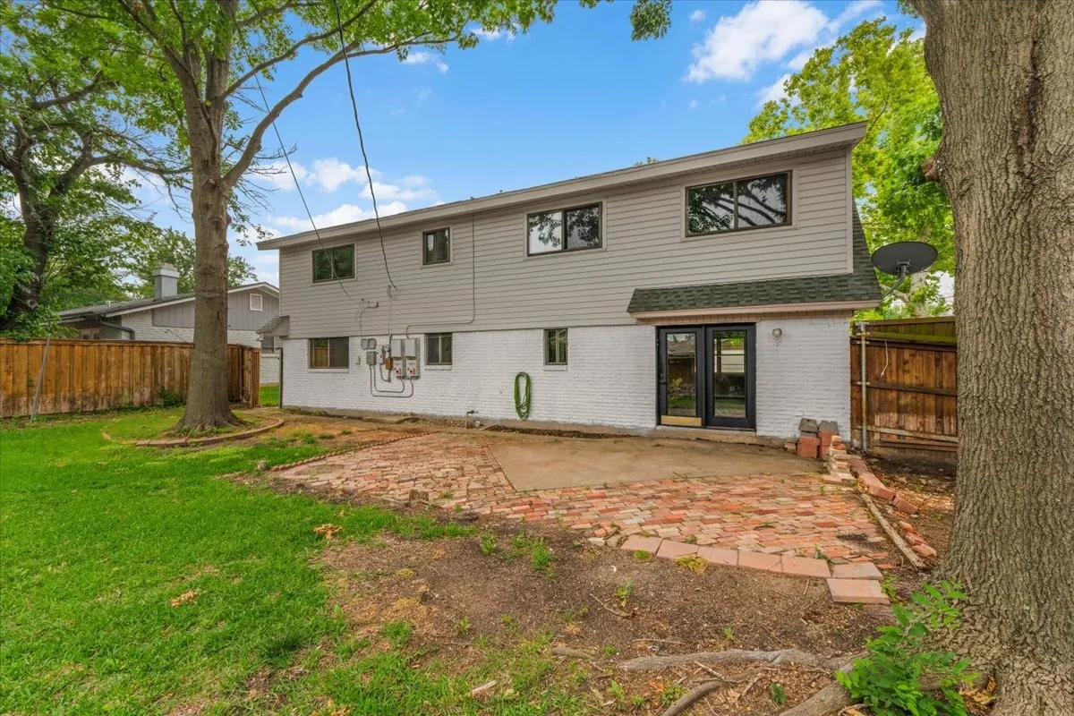 Rear exterior featuring light gray siding over painted white brick, a brick patio, and mature trees