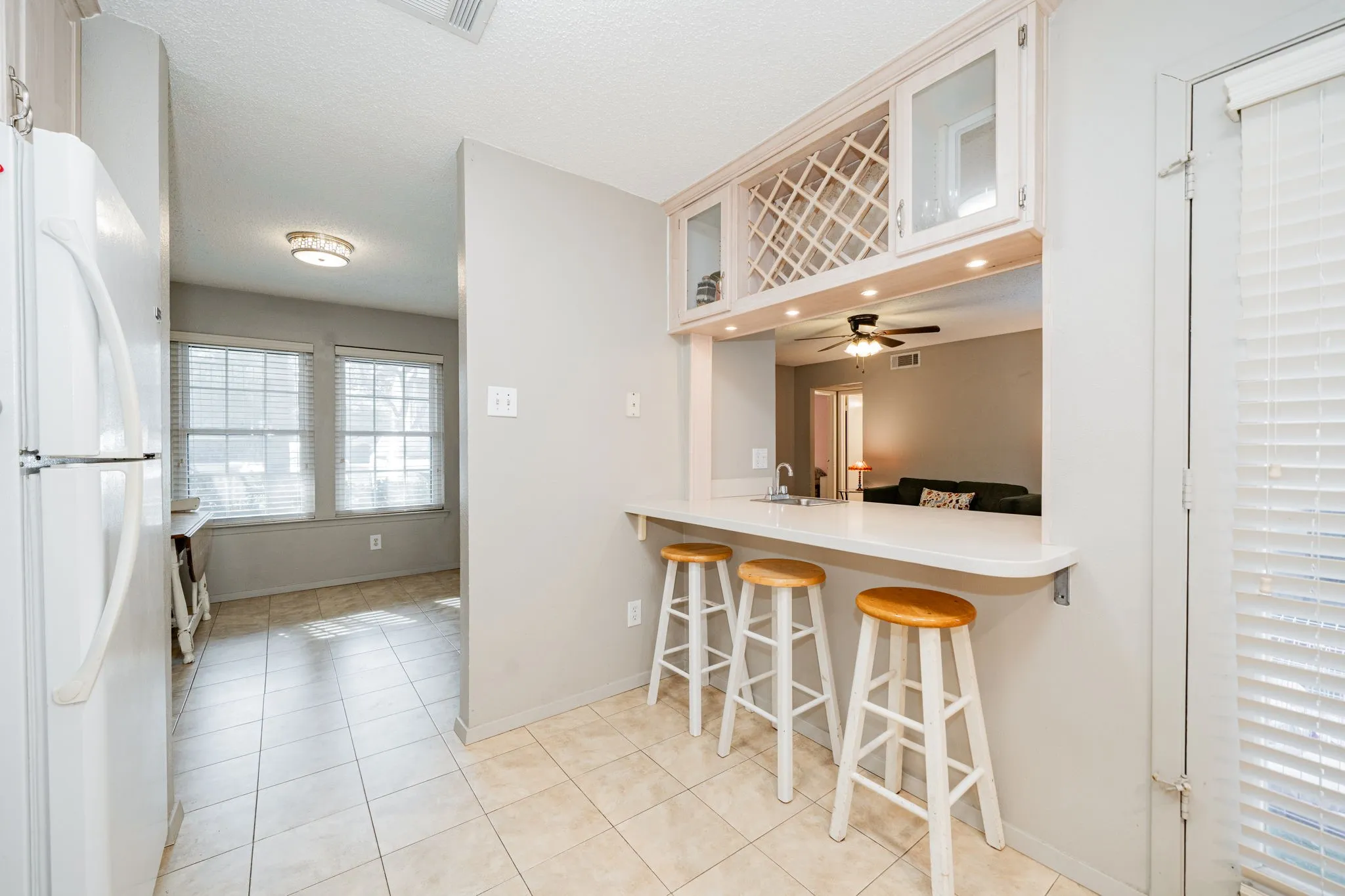 Kitchen pass-through featuring an eating bar, recessed lighting, and upper cabinetry with glass-front display doors and an integrated wine rack
