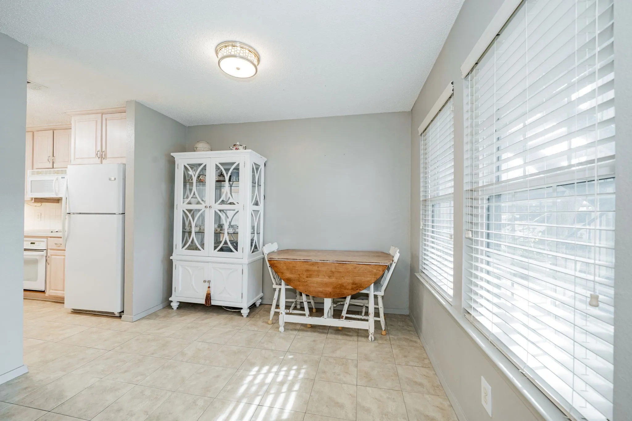 Dining area with tile flooring, two windows featuring blinds, and a ceiling-mounted light fixture