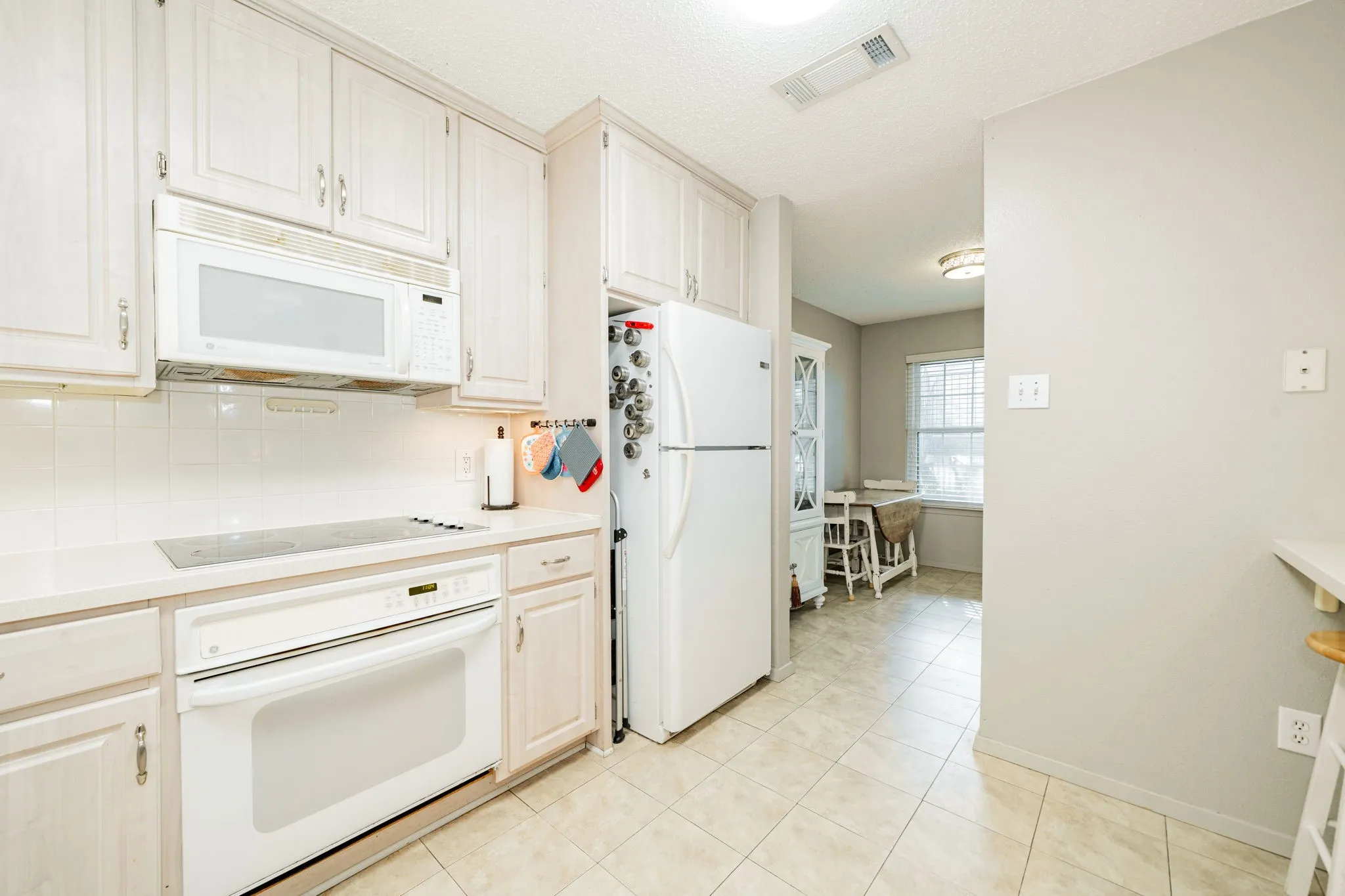Kitchen featuring light wood-finish cabinetry, white appliances, and a tile backsplash