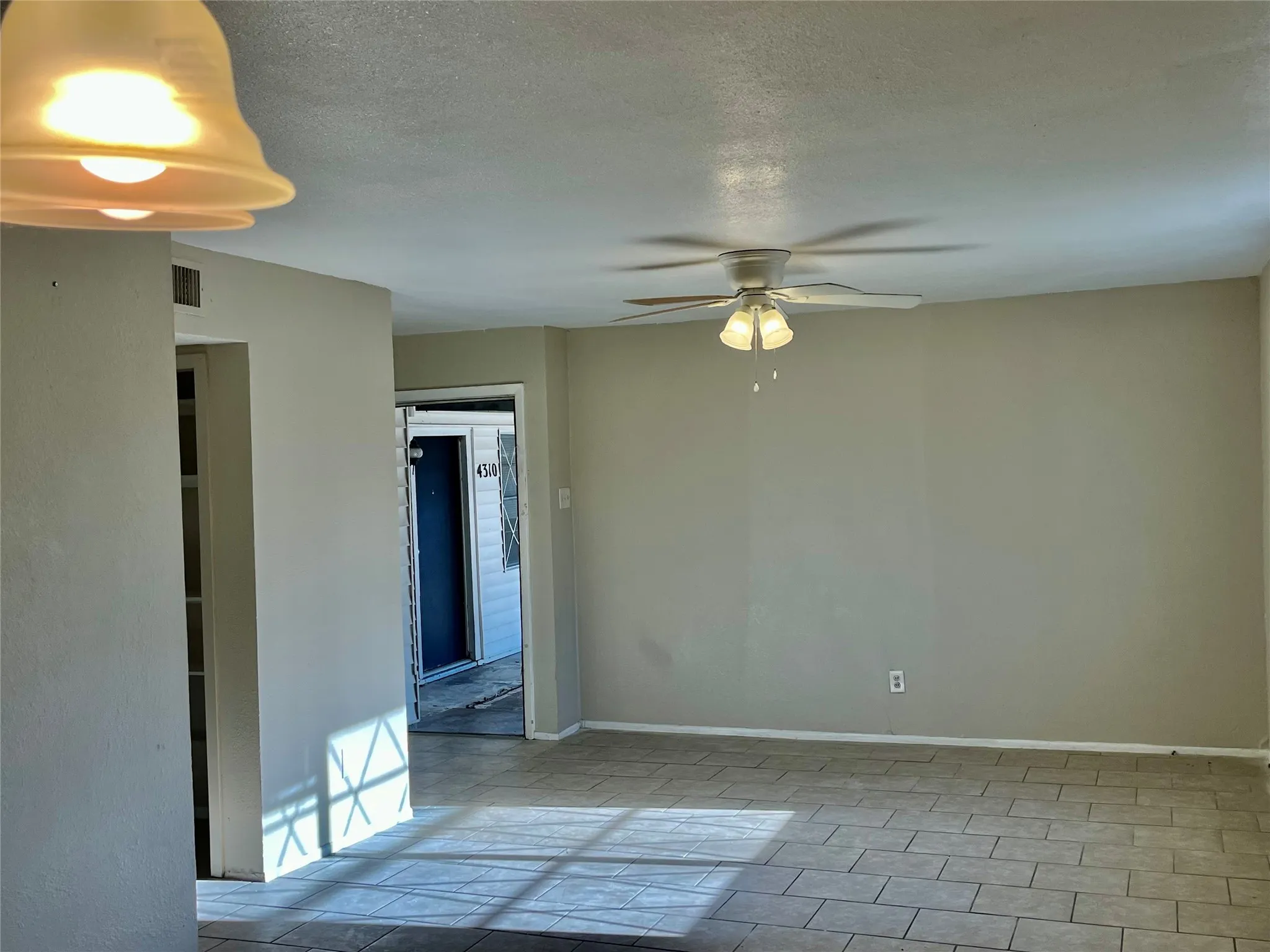 Spacious room featuring neutral wall tones, tile flooring, a ceiling fan with light fixture, and a built-in wall niche