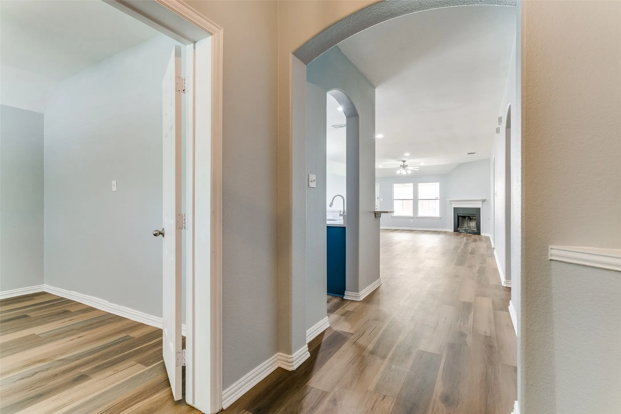 Hallway with wood-finish flooring, featuring an arched entryway and light gray wall paint