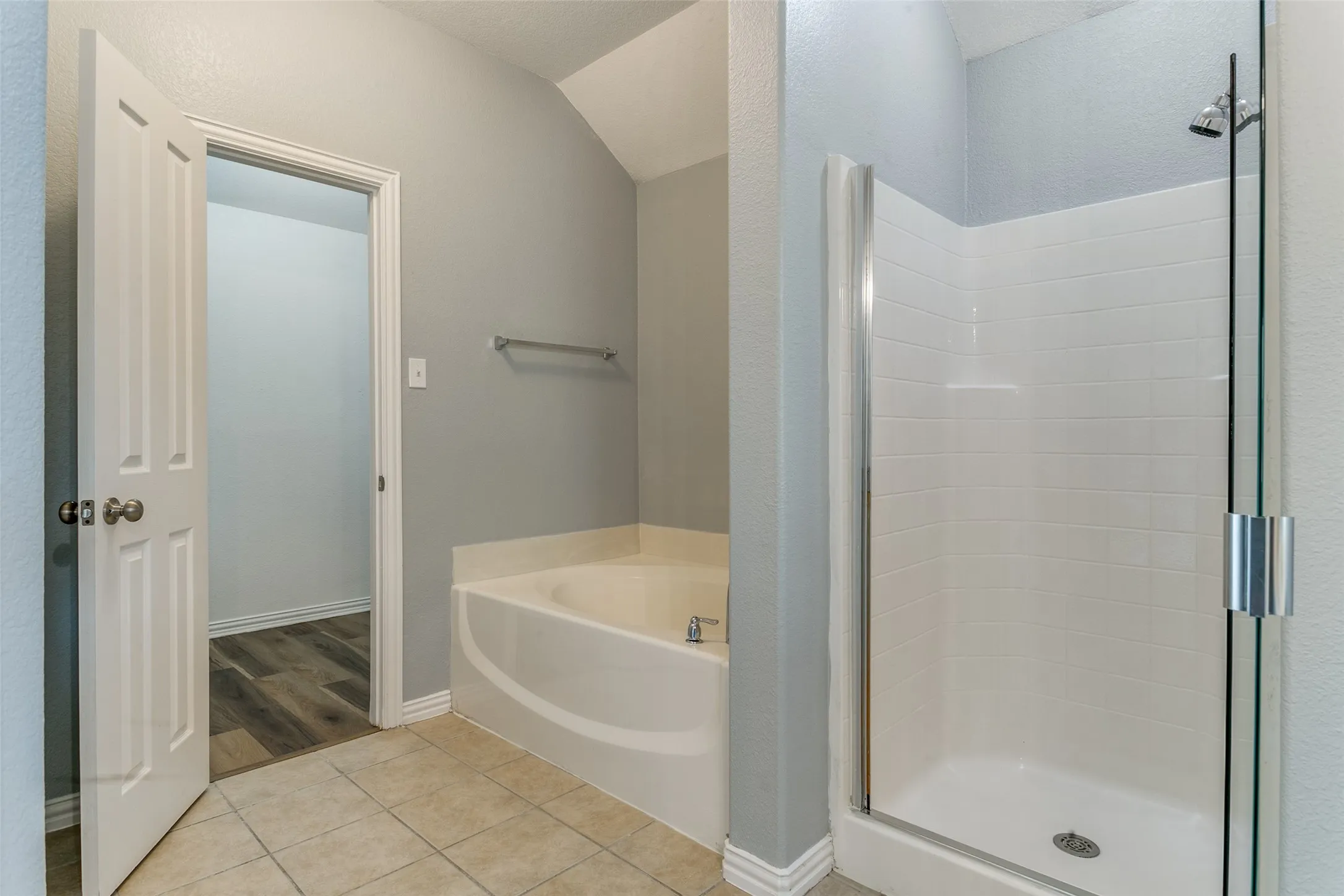 Bathroom featuring a built-in tub, separate shower with a glass enclosure, tile flooring, and vaulted ceiling
