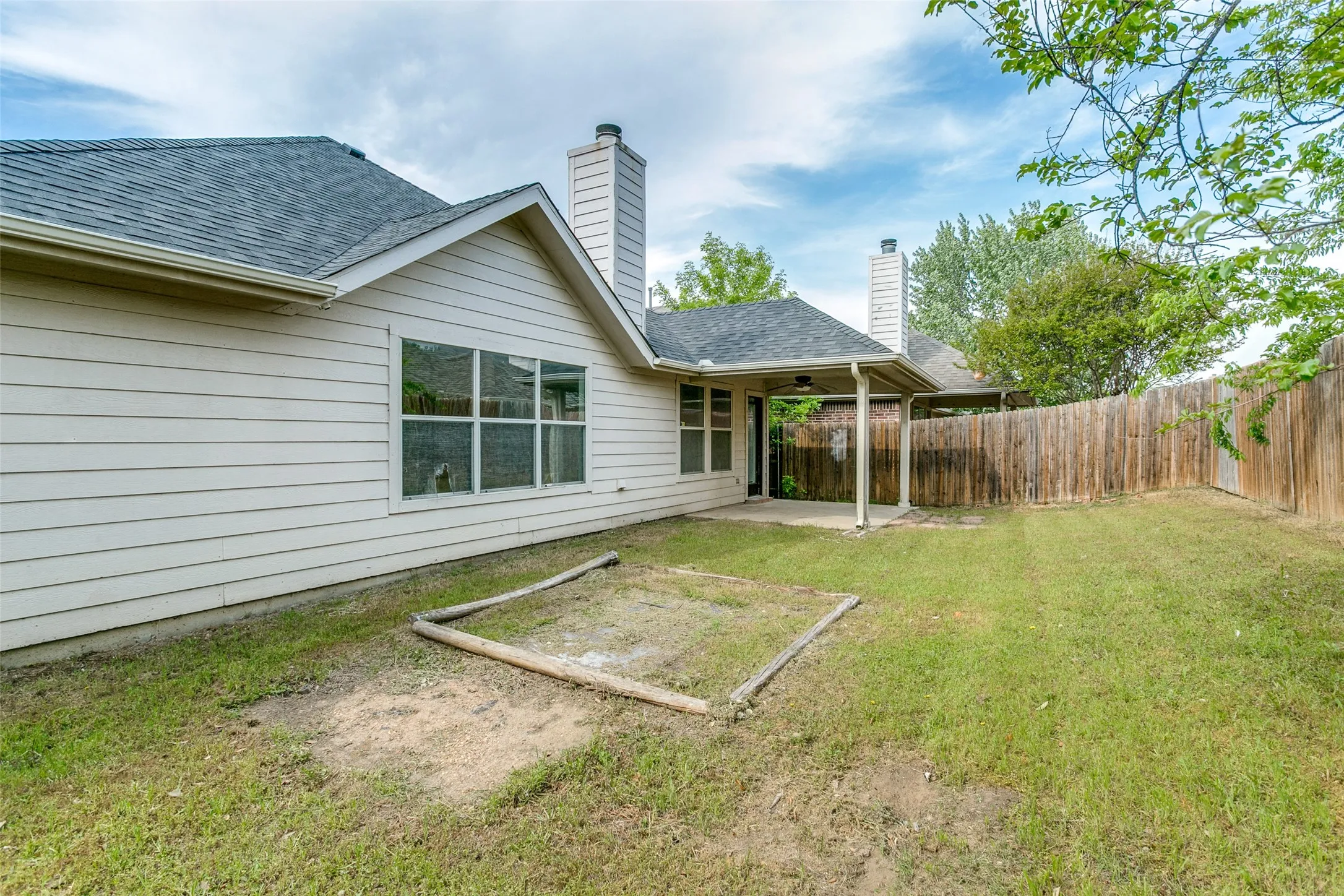 Rear exterior with light-colored horizontal siding, a covered patio, and a wooden privacy fence