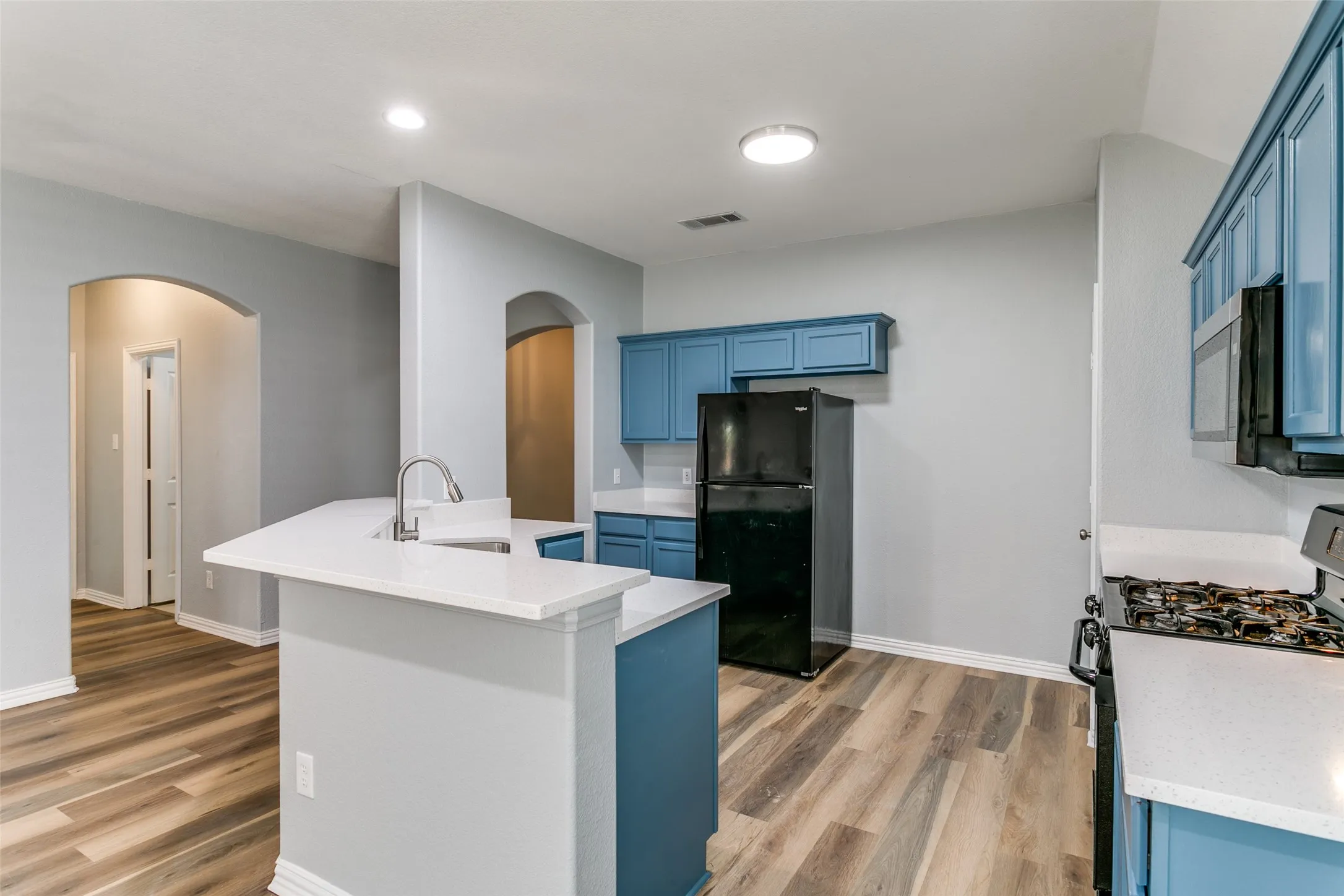 Kitchen featuring blue cabinetry, white countertops, wood-finish flooring, stainless steel appliances, and a kitchen island with an integrated sink