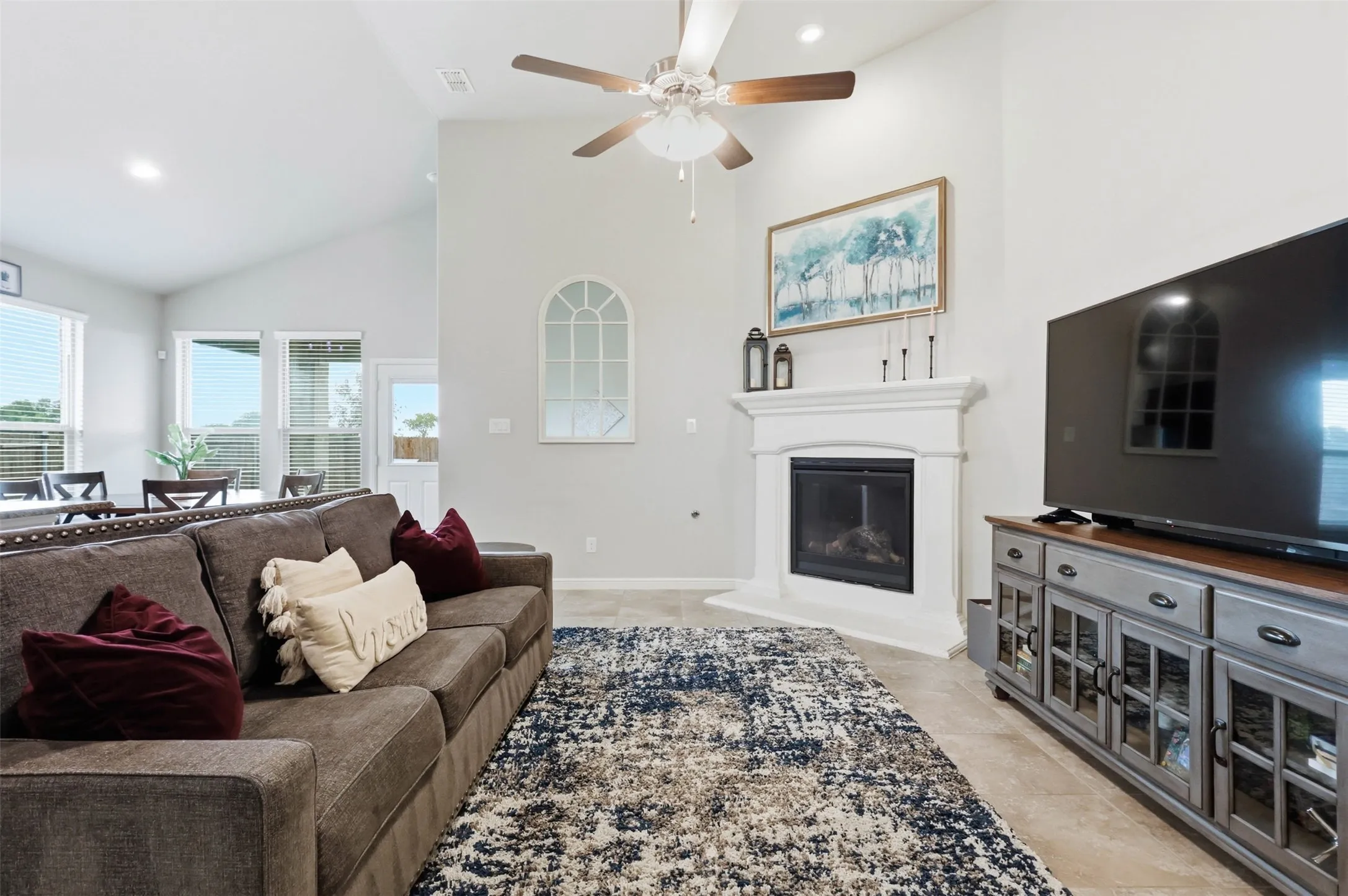 Living area featuring a corner fireplace with a white mantel, vaulted ceilings, a ceiling fan, recessed lighting, and tile flooring