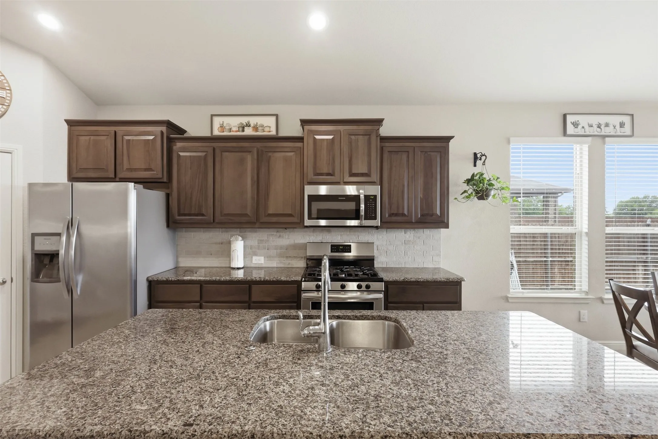 Kitchen featuring granite countertops, stainless steel appliances, wood cabinetry, a tile backsplash, and recessed lighting