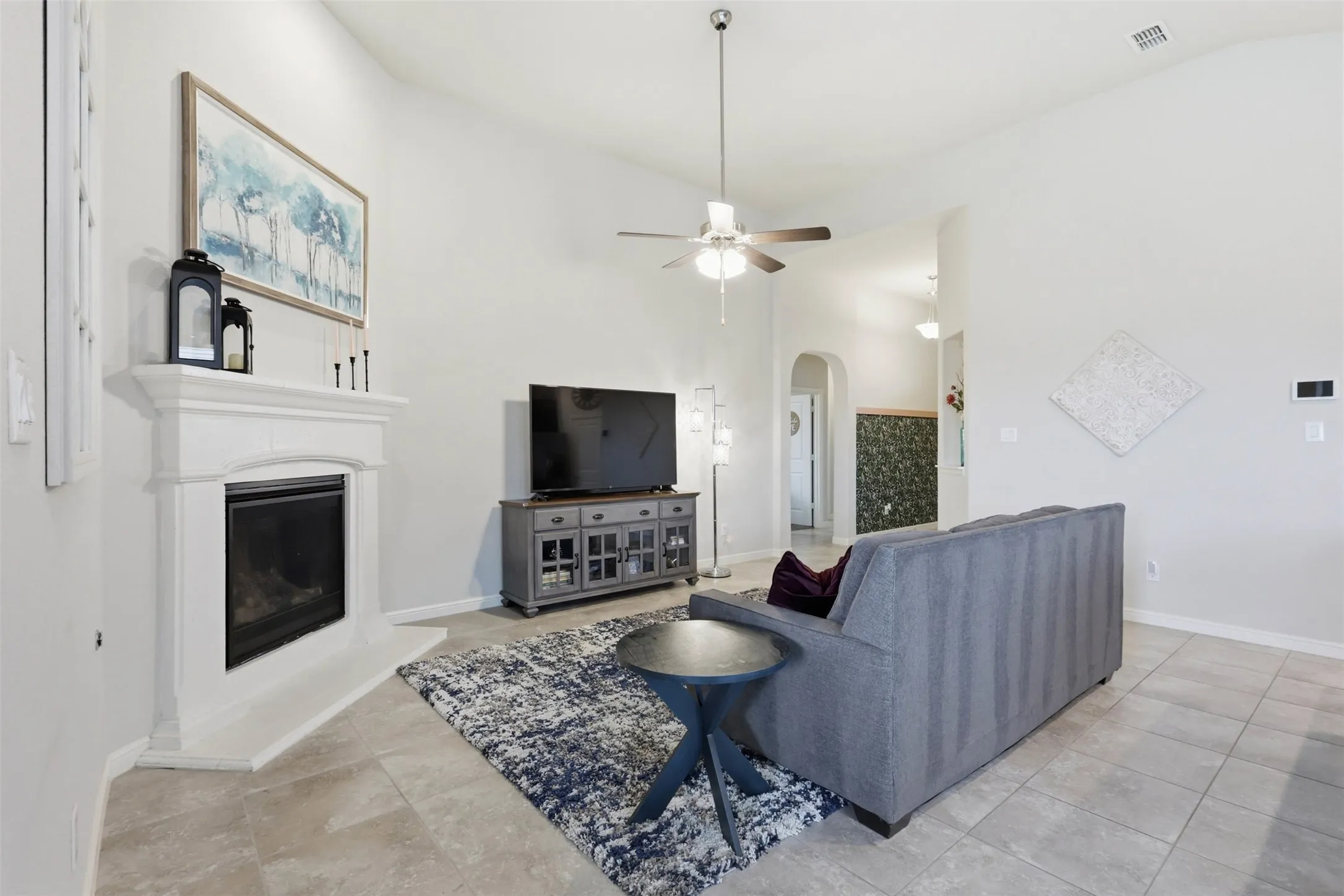Living area featuring a corner fireplace with a white mantel, vaulted ceilings, a ceiling fan, and light-toned tile flooring