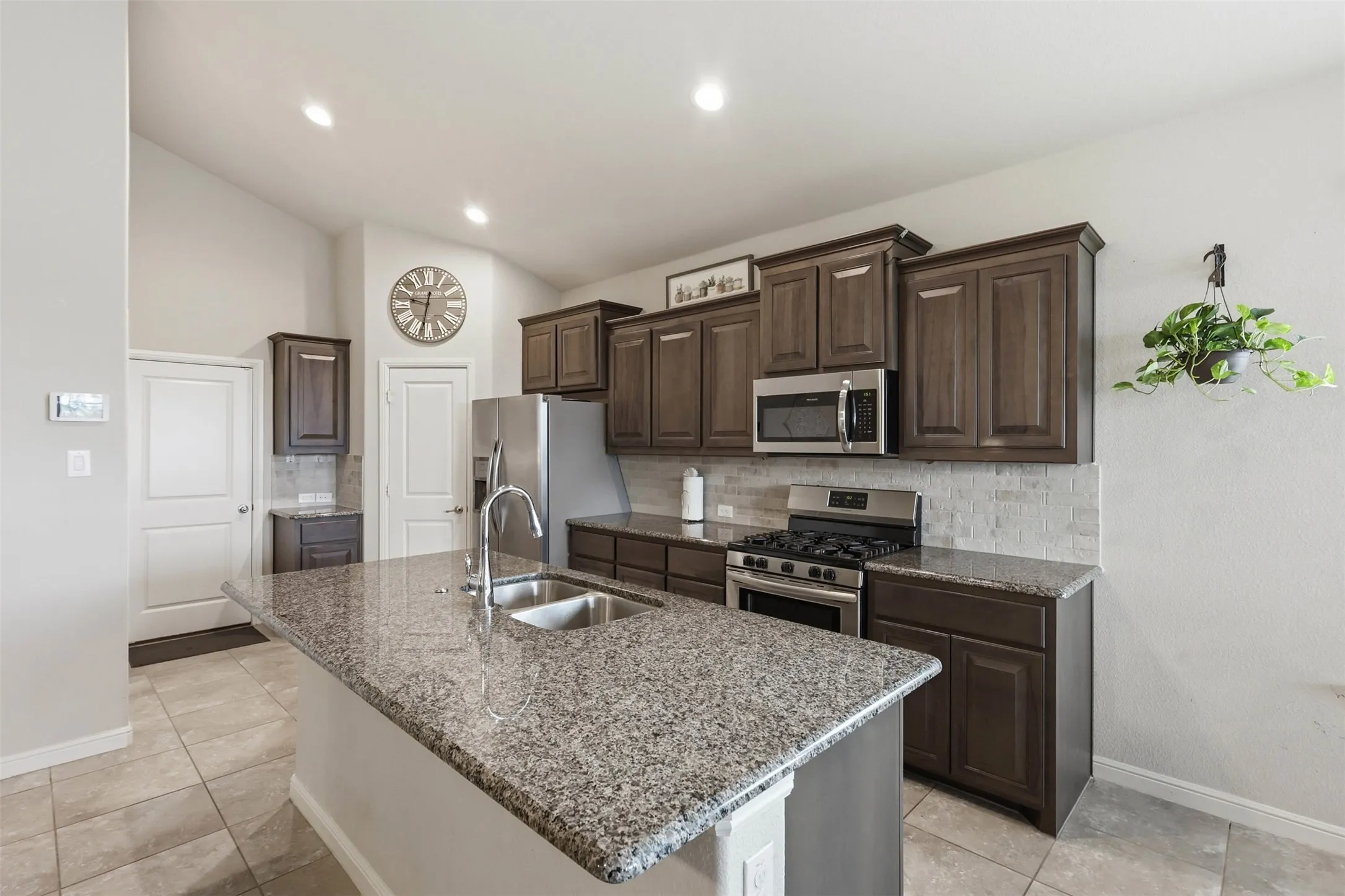 Kitchen featuring a large island with a double basin sink, stainless steel appliances, dark wood-finish cabinetry, and tiled flooring