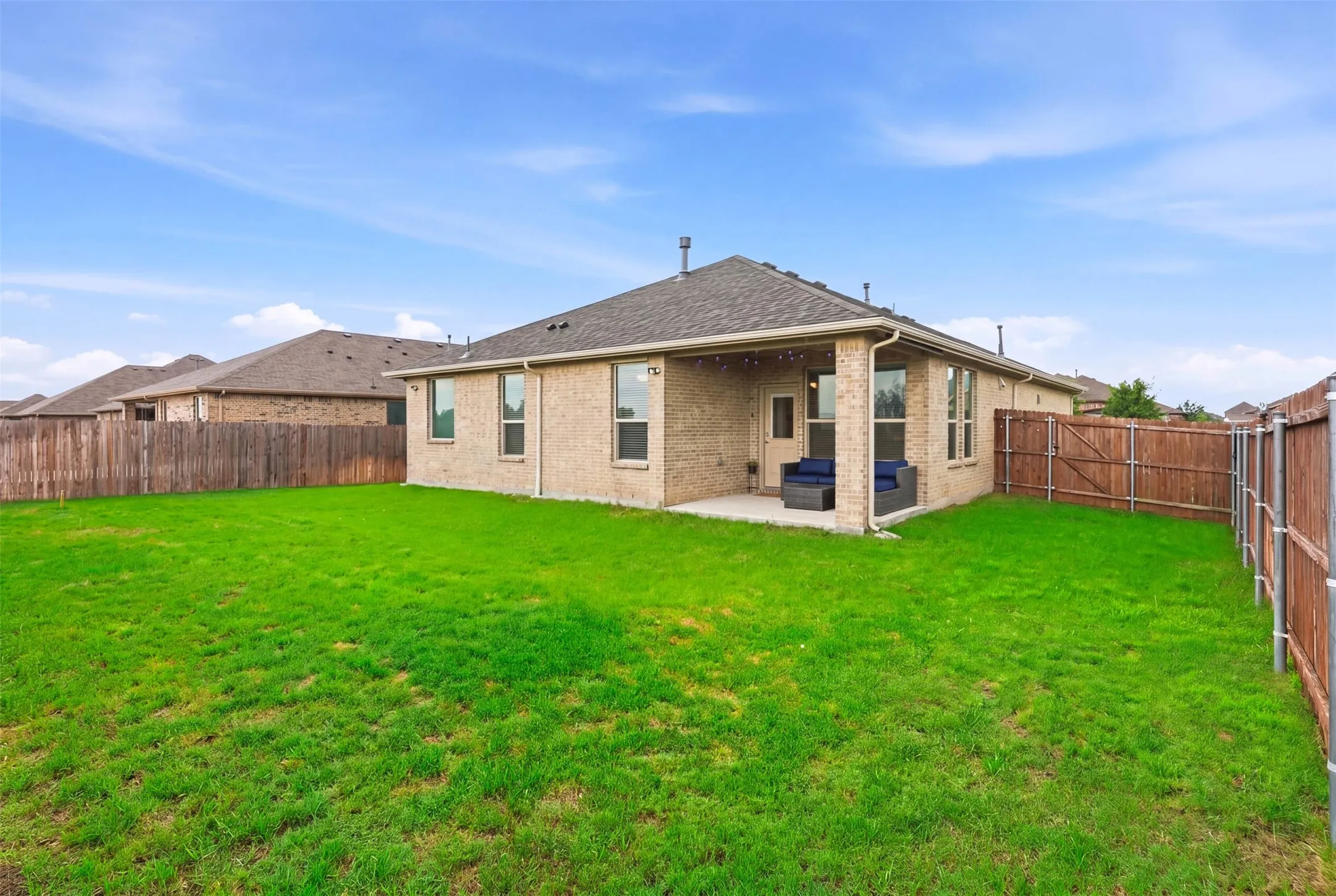 Expansive backyard featuring a lush lawn, privacy fencing, and a covered concrete patio