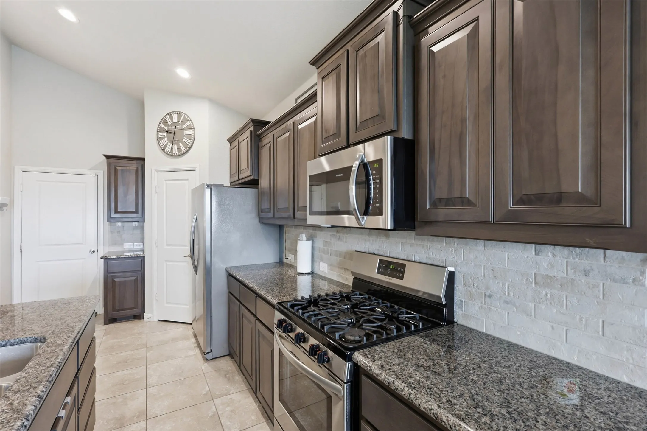 Kitchen featuring dark wood-finish cabinetry, speckled stone countertops, and a subway tile backsplash
