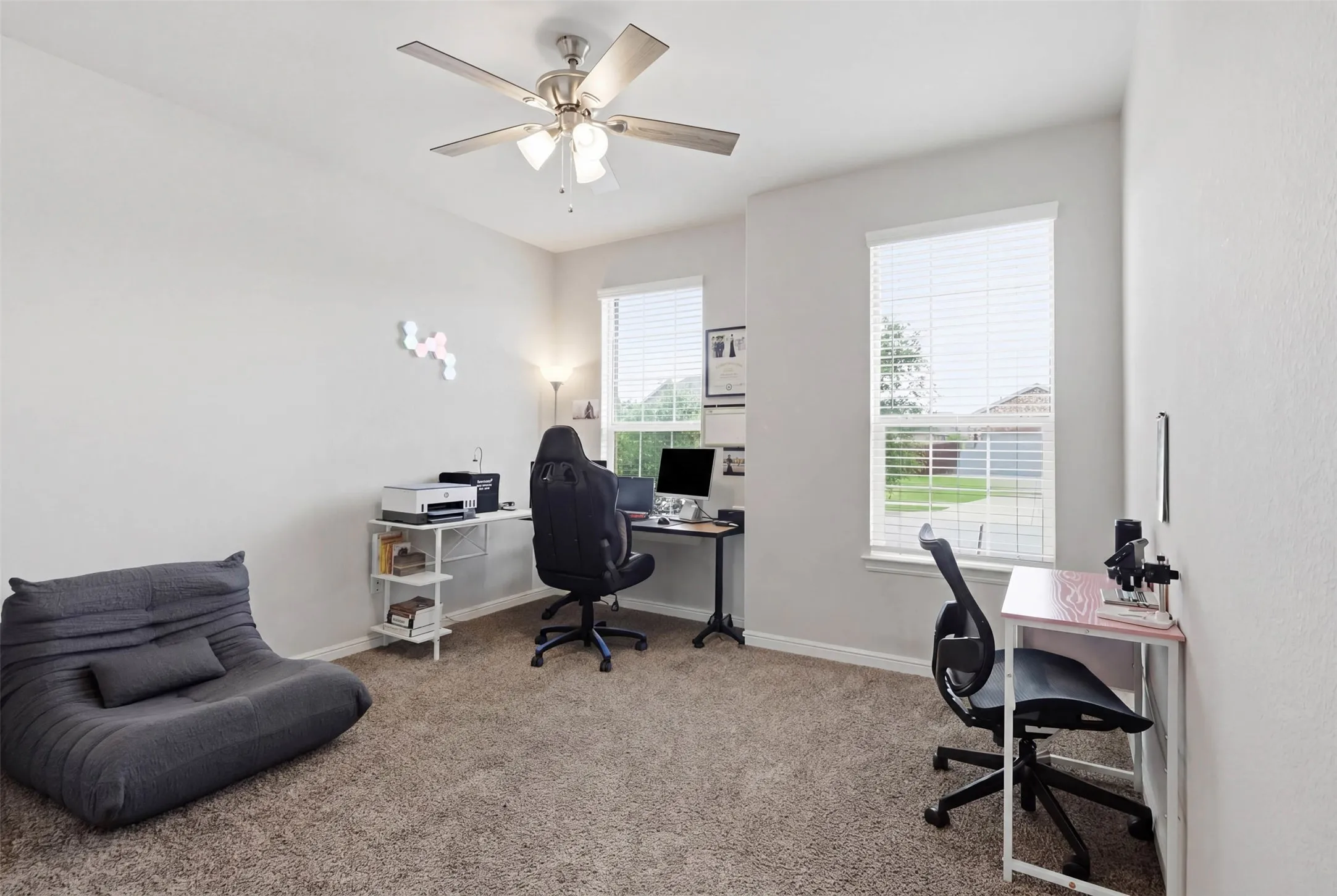 Carpeted room featuring multiple windows with blinds, a ceiling fan with integrated lighting, and neutral wall tones