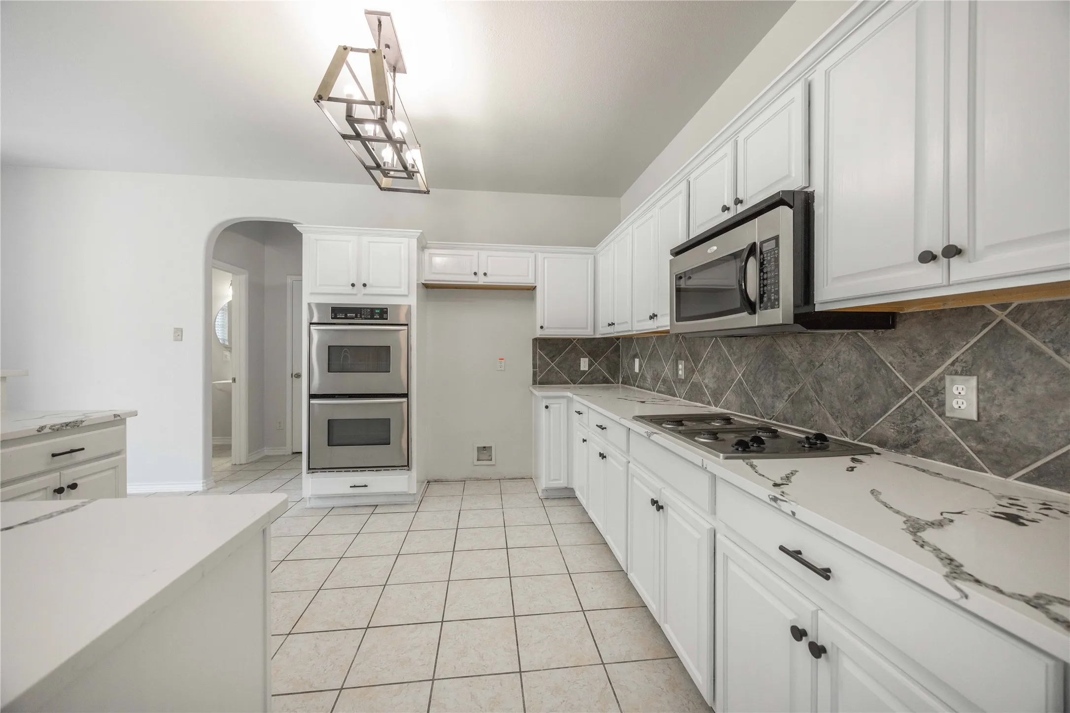 Modern kitchen featuring white cabinetry, stainless steel appliances, patterned tile backsplash, and light-toned countertops