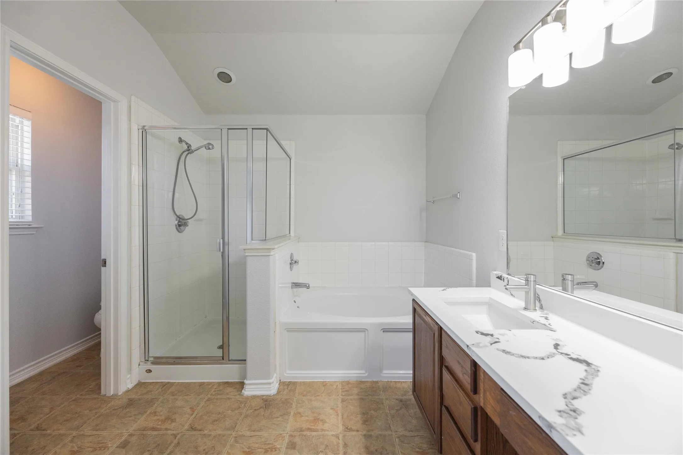 Spacious bathroom featuring a double vanity with a stone countertop, a separate glass-enclosed shower, a built-in tub, tile flooring, and a large wall-mounted mirror