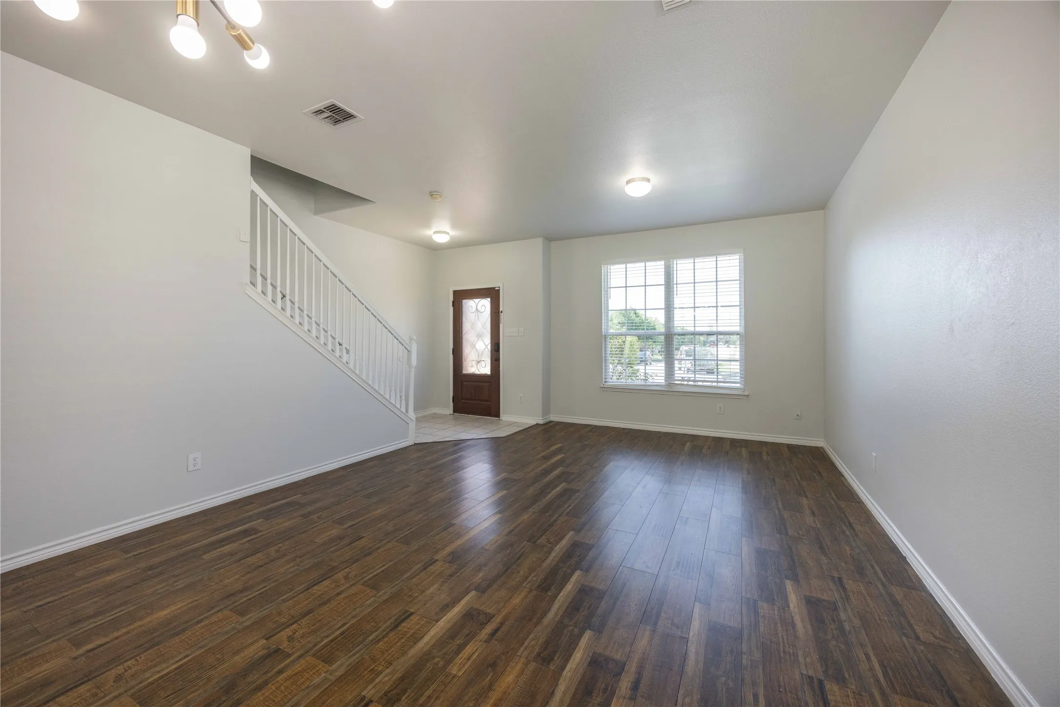 Spacious room featuring wood-finish flooring, light gray walls, and a large window with white blinds