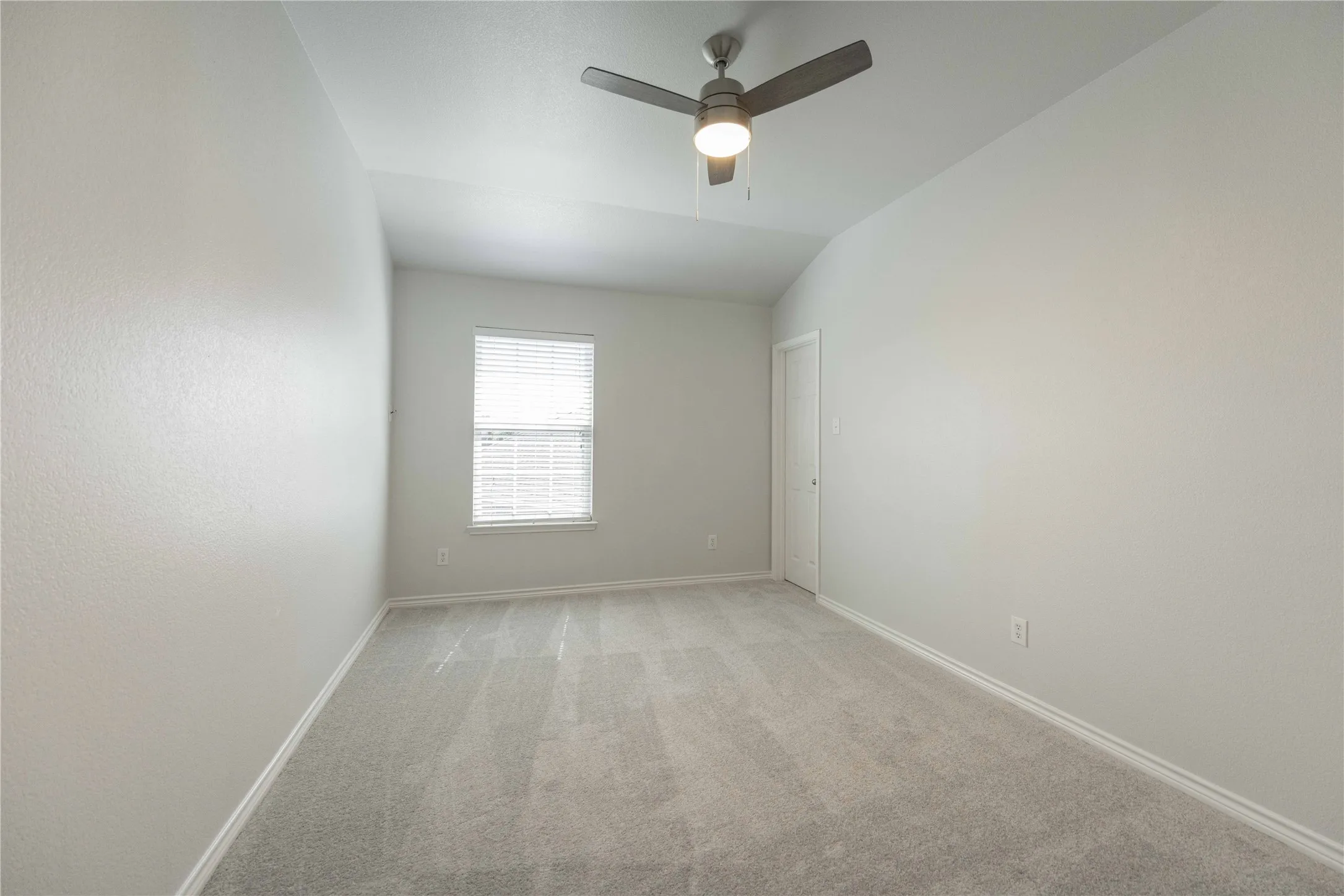 Carpeted room featuring a ceiling fan with integrated lighting, a window with blinds, and a white interior door