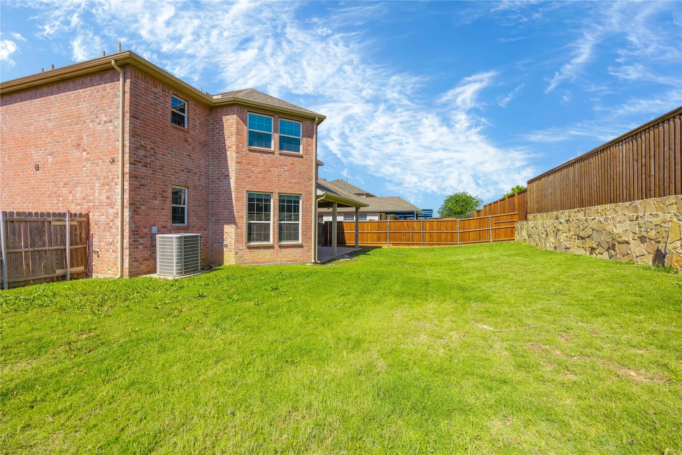 Spacious backyard featuring a manicured lawn, full brick exterior, a covered patio, and a stone retaining wall