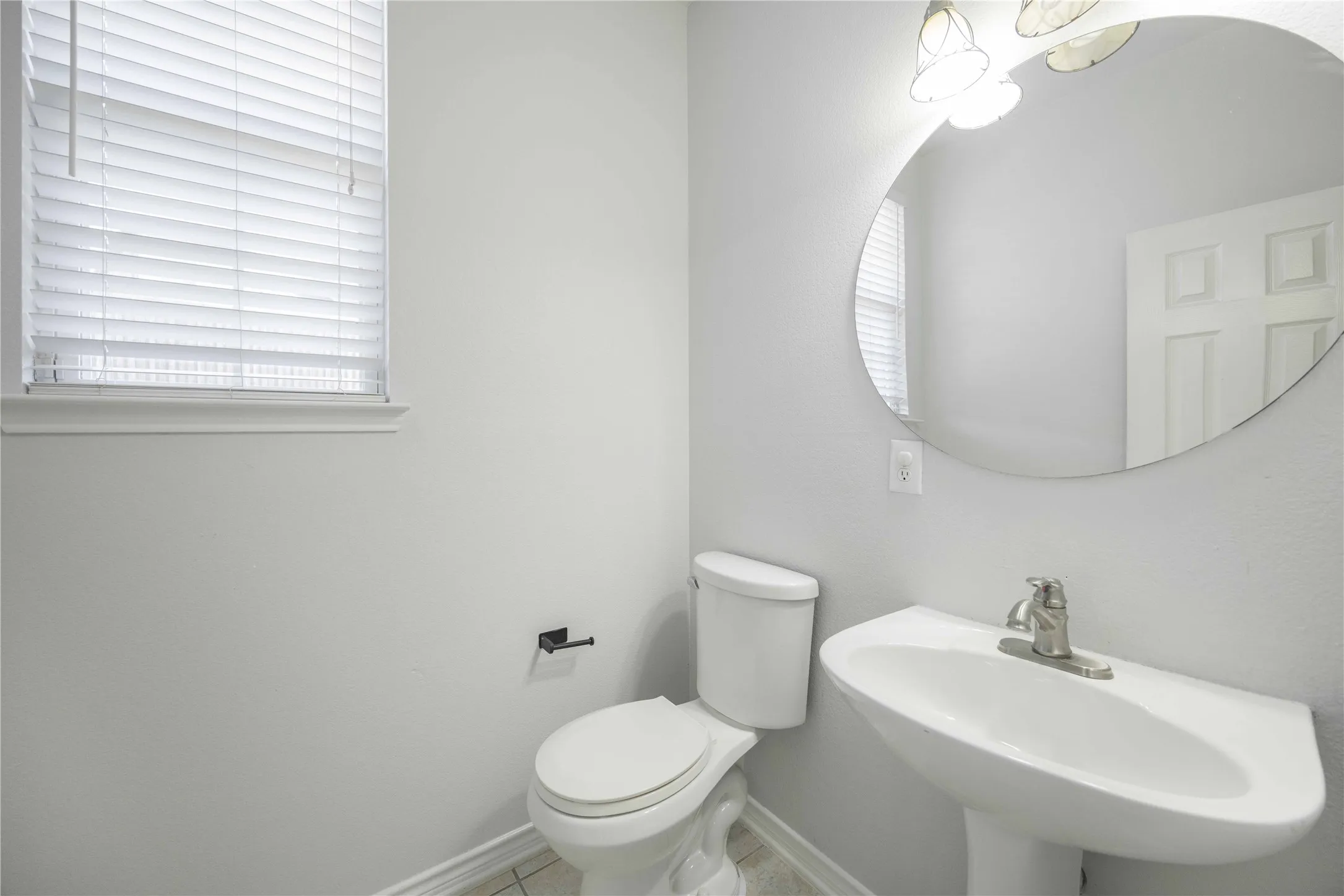Pedestal sink with a single-handle faucet, circular mirror, and overhead vanity lighting