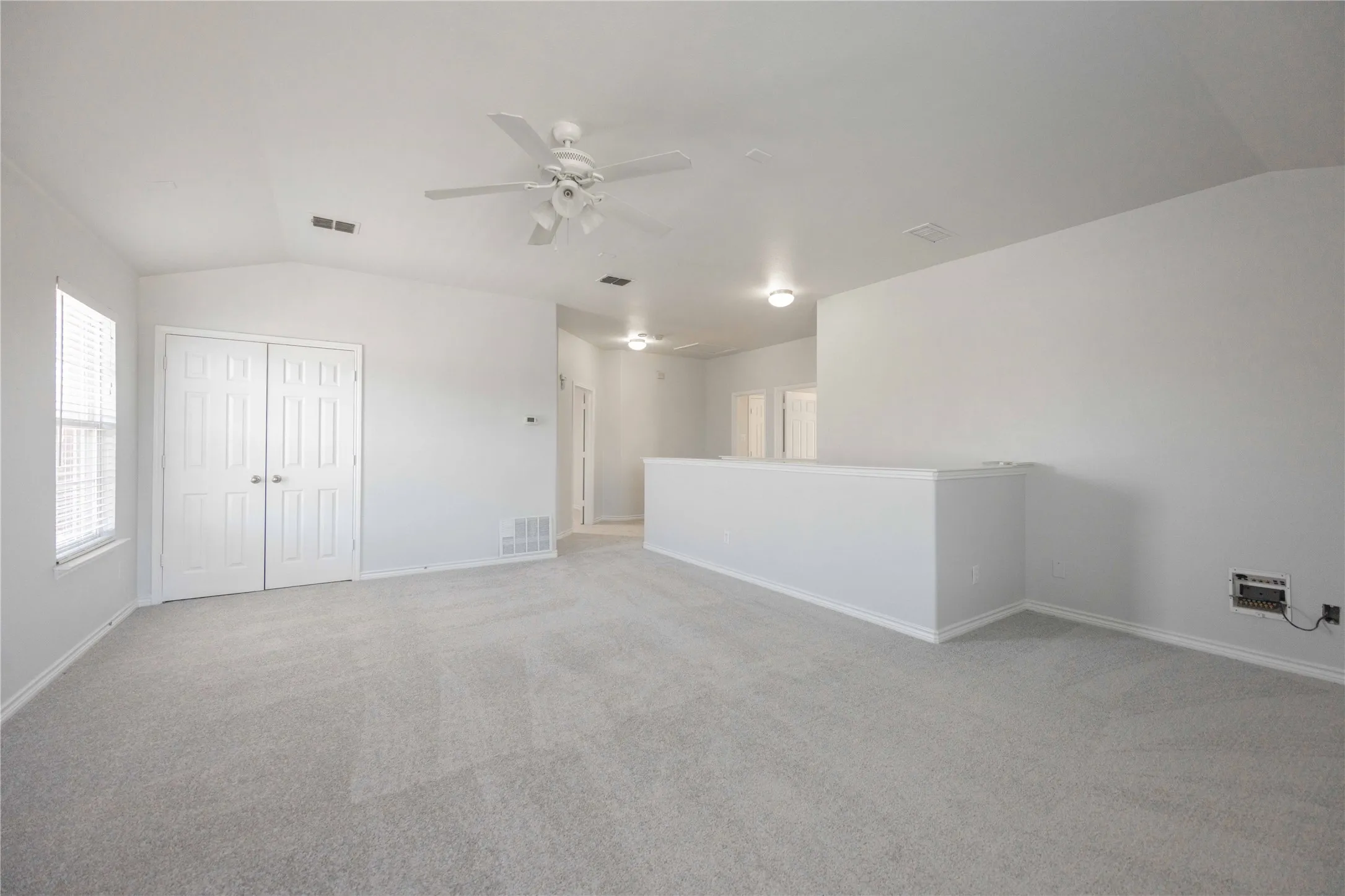 Spacious room featuring vaulted ceilings, light-tone carpeting, a ceiling fan, and double-pane window with blinds