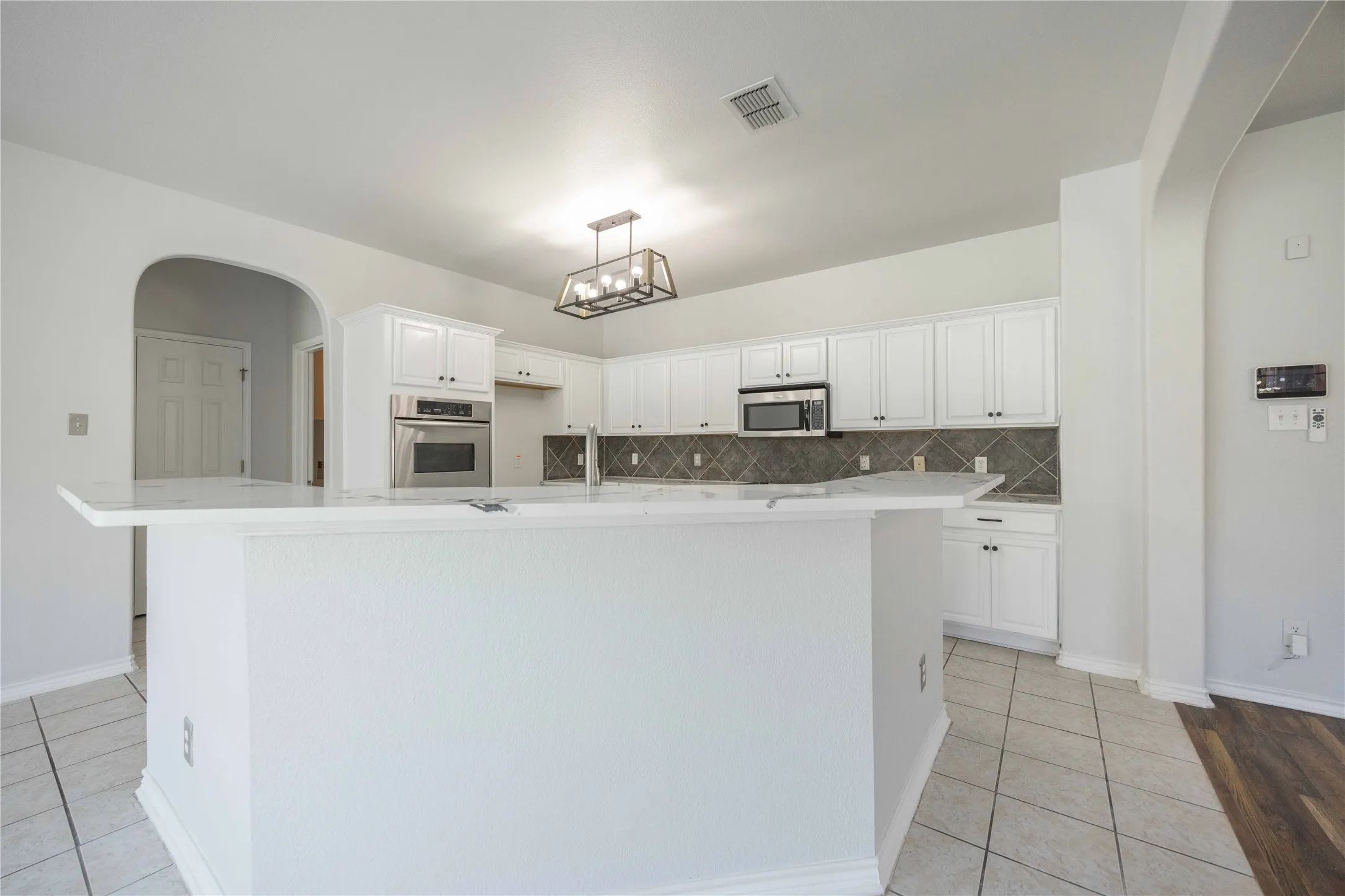 Kitchen featuring a central island with white countertop, white cabinetry, integrated stainless steel oven, and microwave