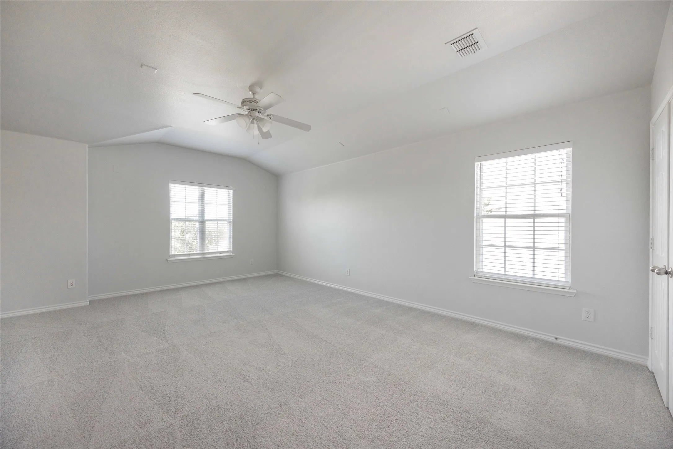 Spacious room featuring vaulted ceilings, light gray carpeting, and two windows with blinds