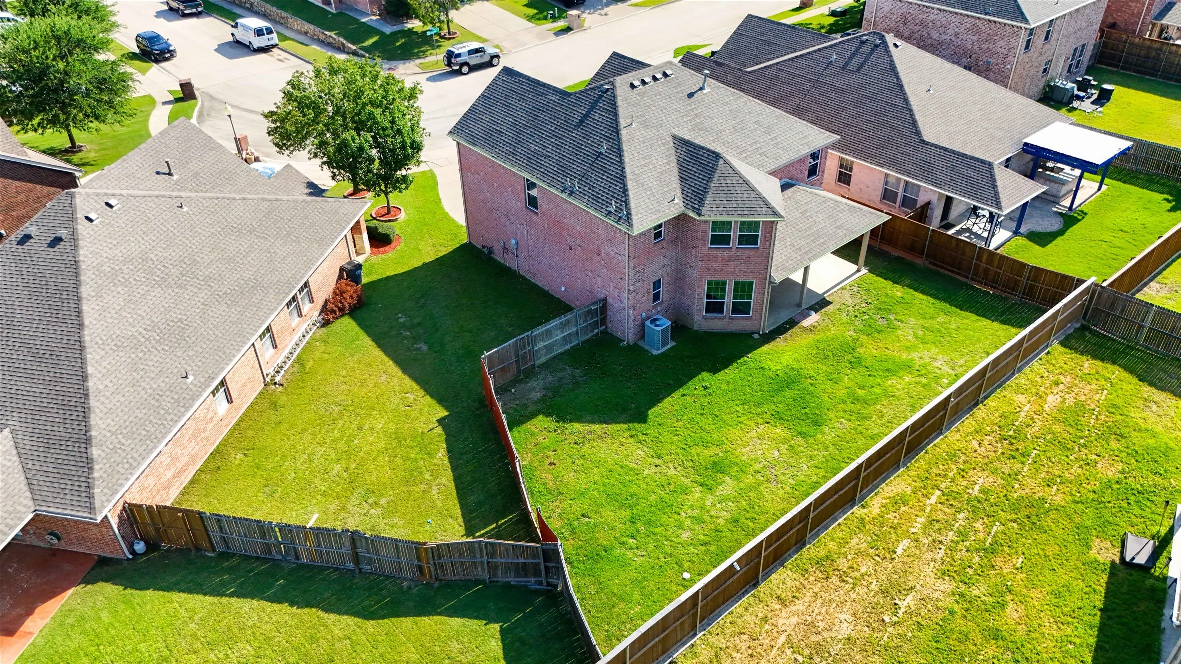 Expansive fenced backyard featuring a covered patio, manicured lawn, and brick exterior