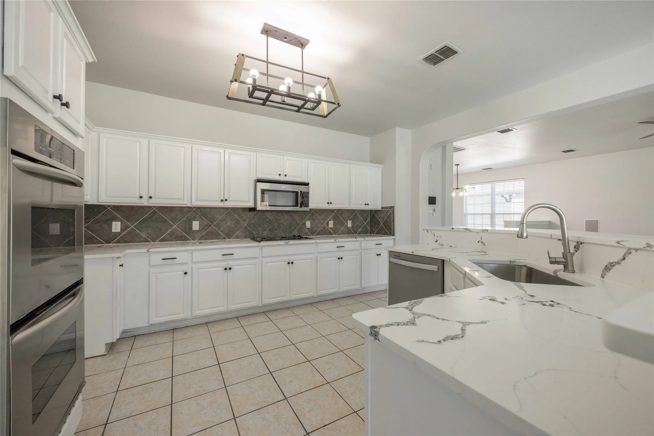 Contemporary kitchen featuring white cabinetry, stainless steel appliances, a diamond-patterned backsplash, and light-toned tile flooring