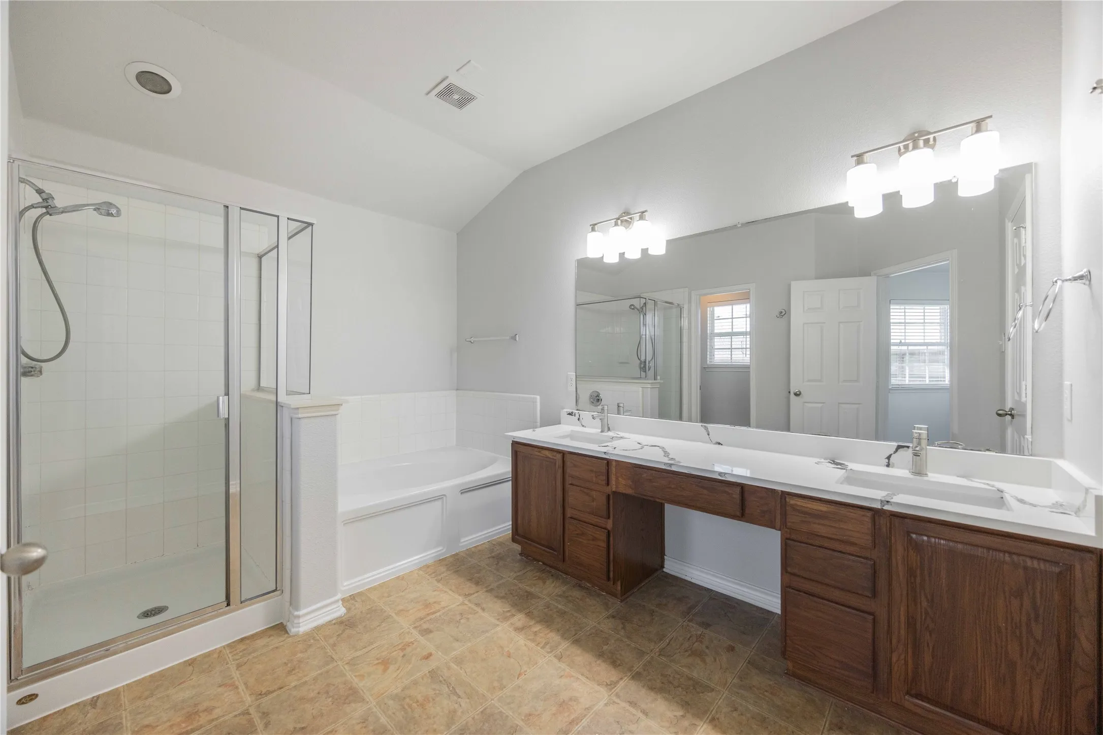 Bathroom featuring a glass-enclosed shower, a built-in tub, and a dual vanity with a long countertop