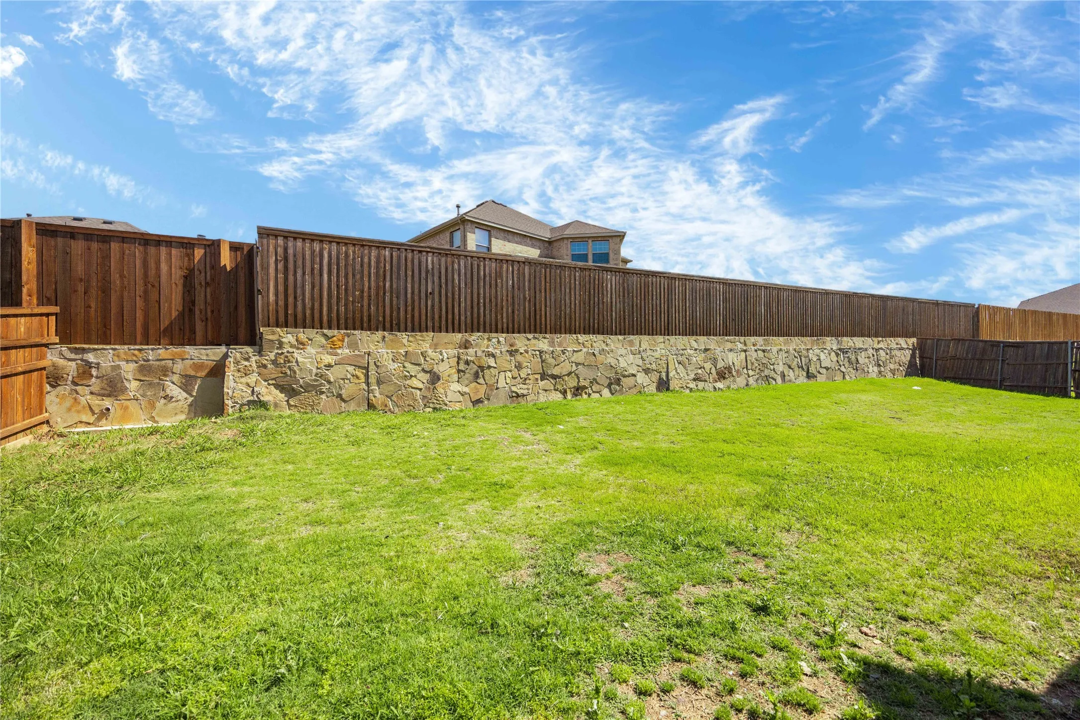 Expansive backyard featuring a stone retaining wall topped with a wood privacy fence, providing definition and enclosure