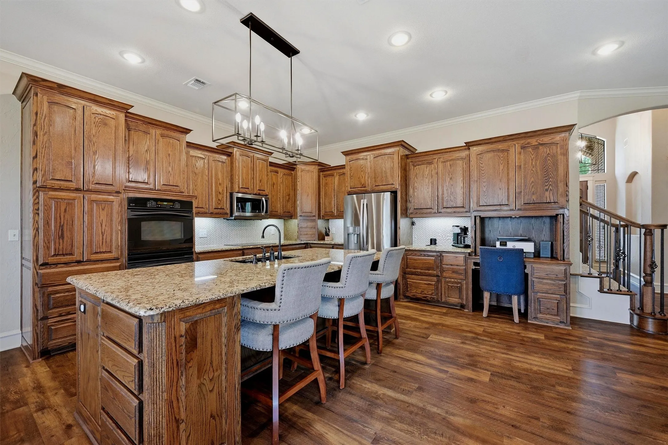 Gourmet kitchen featuring extensive wood cabinetry, granite countertops, built-in stainless steel appliances, a central island with seating, and wood-finish flooring