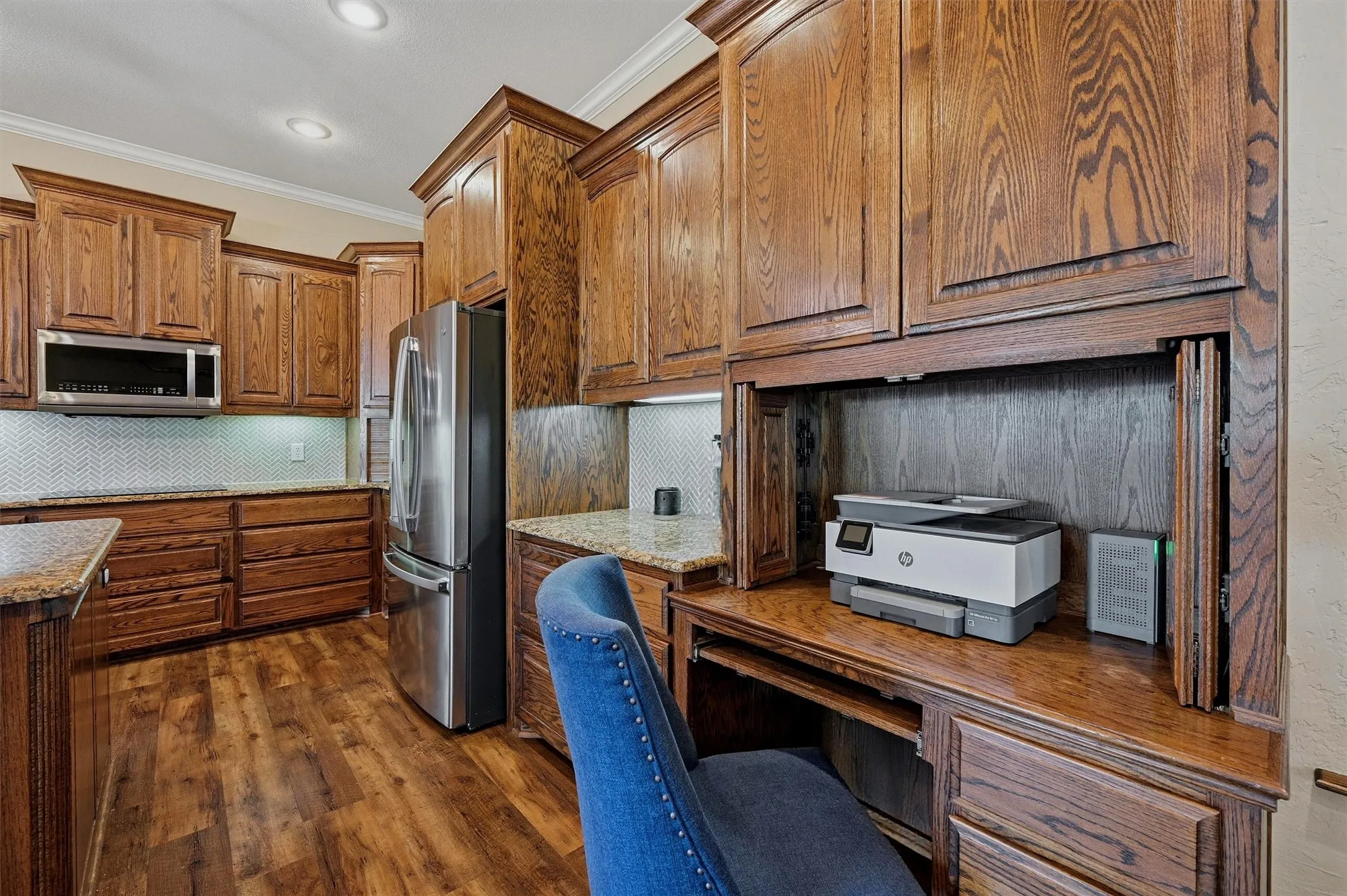 Custom wood-finish cabinetry providing ample storage, integrated stainless steel appliances, granite countertops, and a full tile backsplash