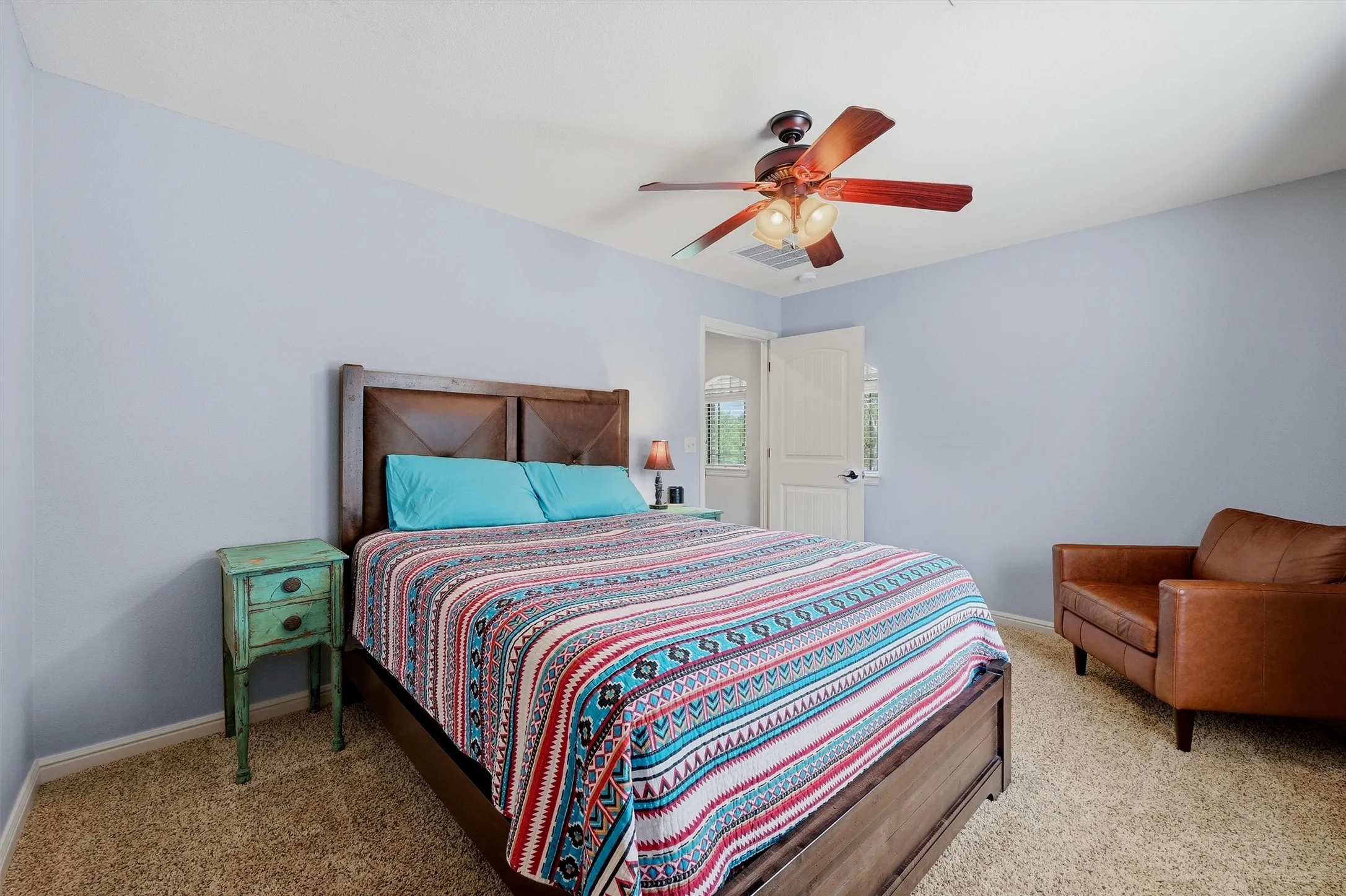 Carpeted bedroom with a wood-finish bed frame, light blue wall paint, and a ceiling fan with integrated lighting