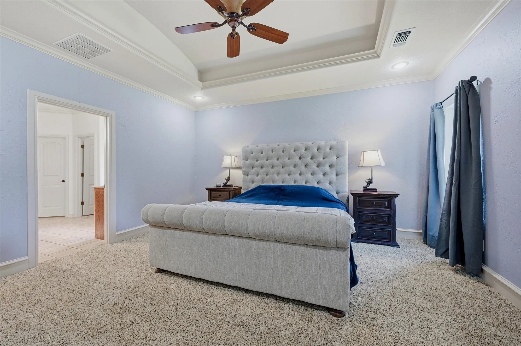 Recessed lighting and a ceiling fan illuminate this space featuring a tray ceiling, crown molding, and carpet flooring
