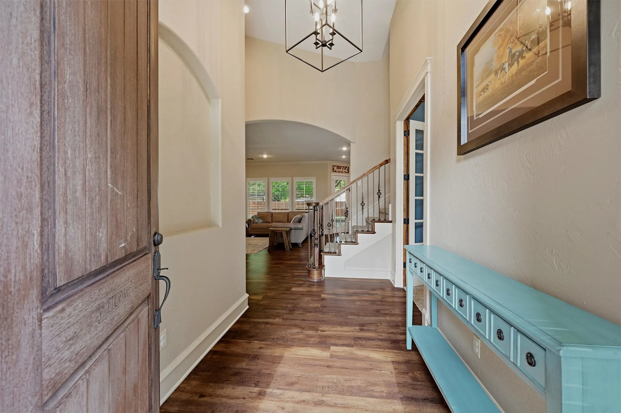 Foyer featuring wood-finish flooring, a contemporary chandelier, arched entryways, and a staircase with wrought iron balusters
