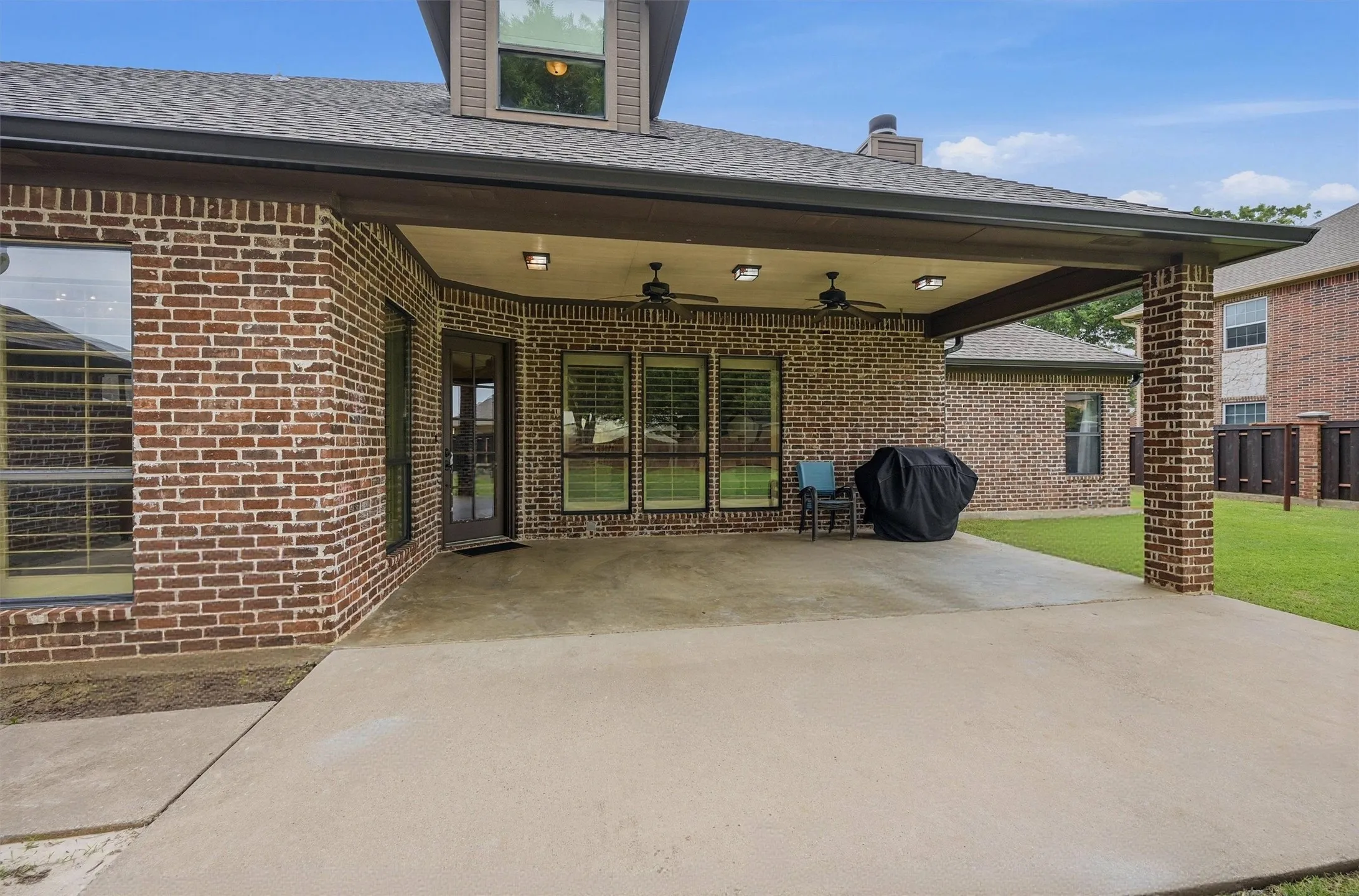 Expansive concrete patio beneath a covered porch, featuring brick columns and brick exterior