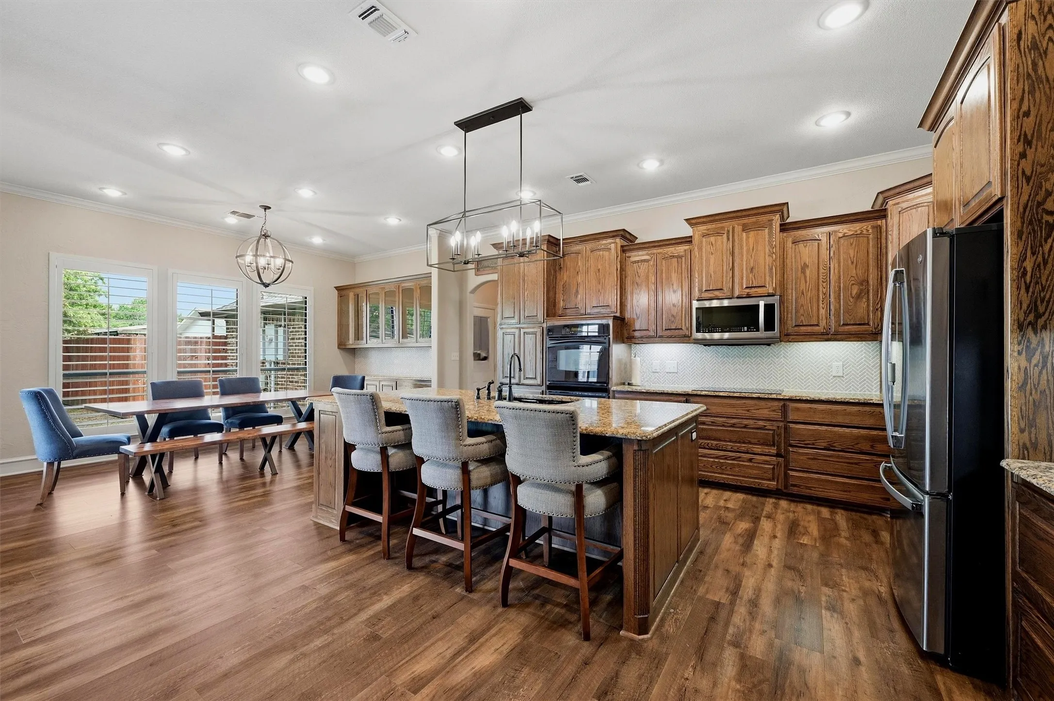 Spacious kitchen featuring wood-finish flooring, custom wood cabinetry, stainless steel appliances, and a large island with a stone countertop