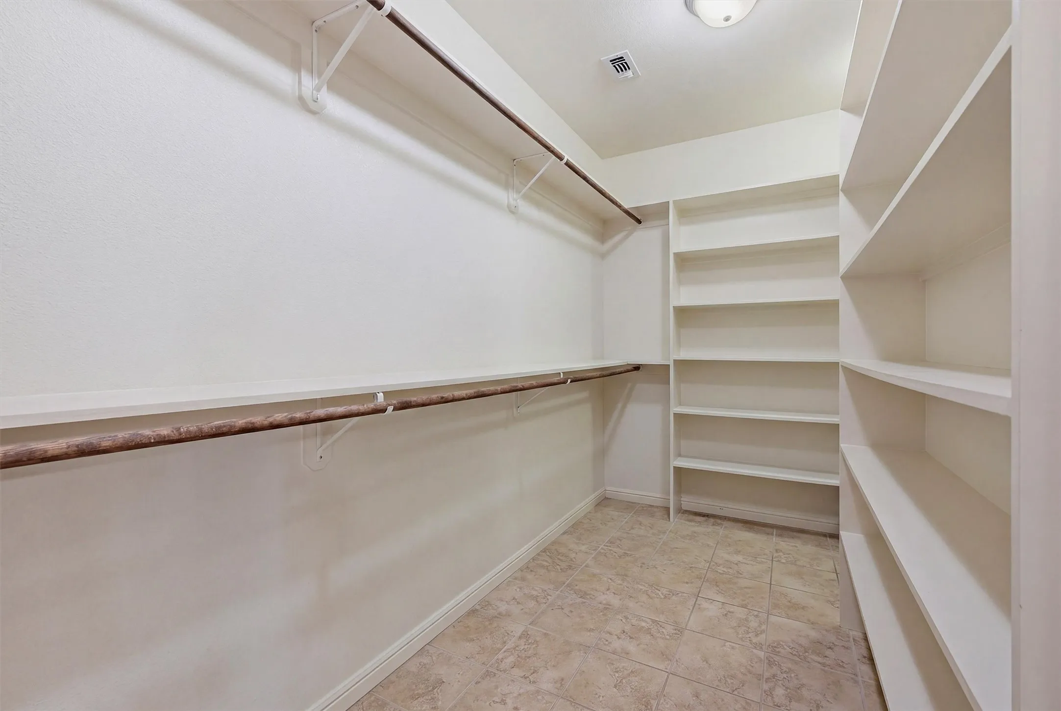 Walk-in closet featuring floor-to-ceiling shelving, multiple hanging rods, and tile flooring