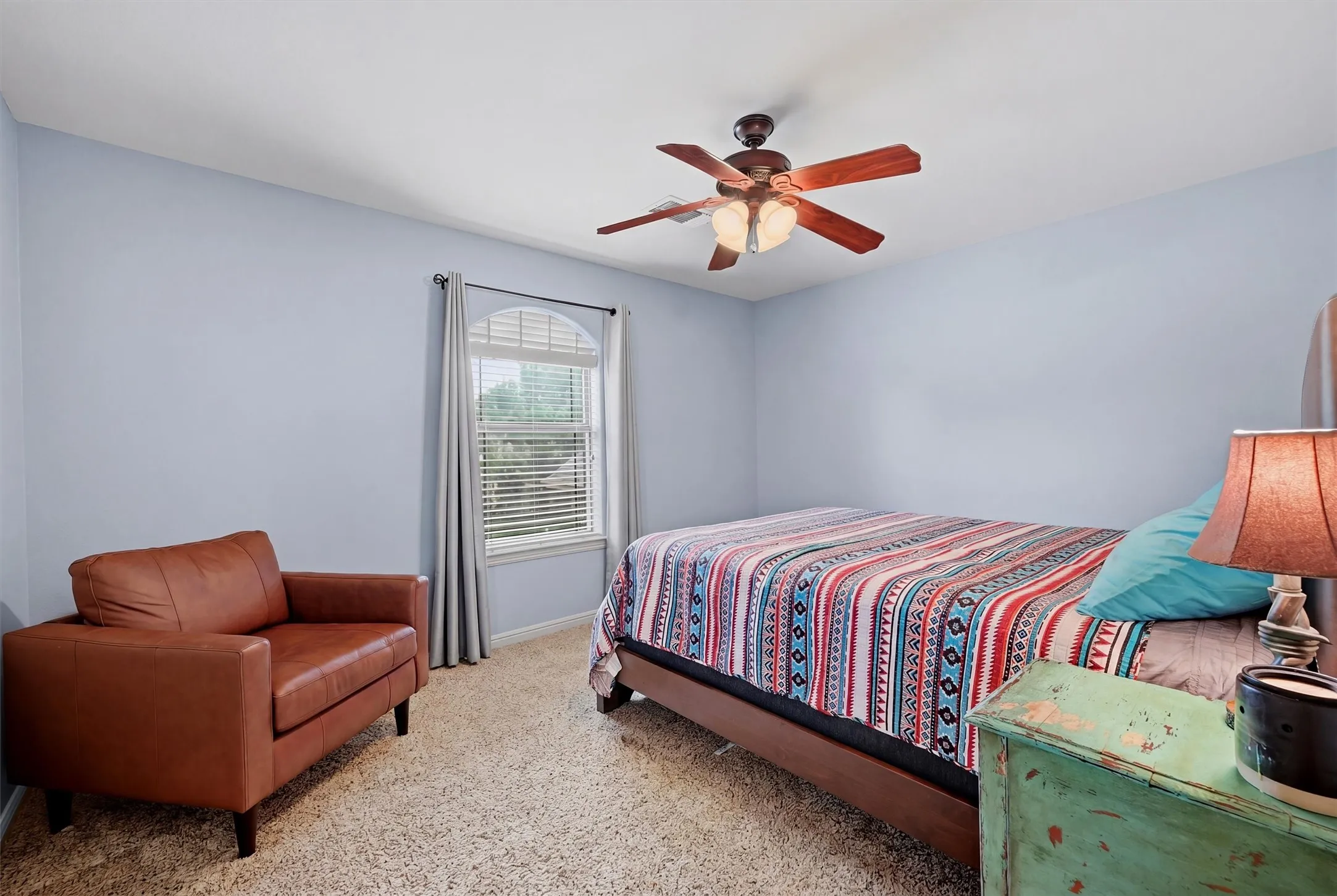 Bedroom featuring a ceiling fan, carpet flooring, and an arched window with blinds