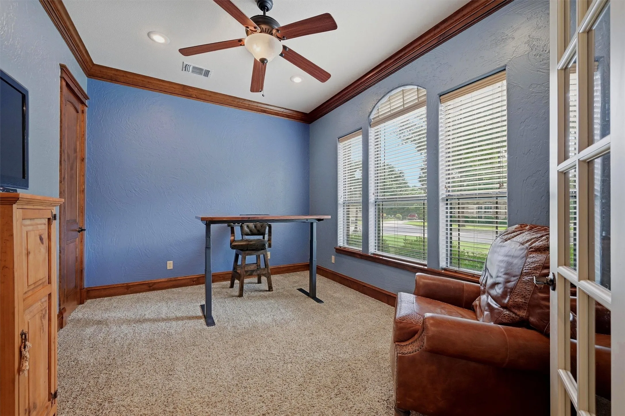 French doors opening to a room with textured blue walls, wood trim, and carpet flooring