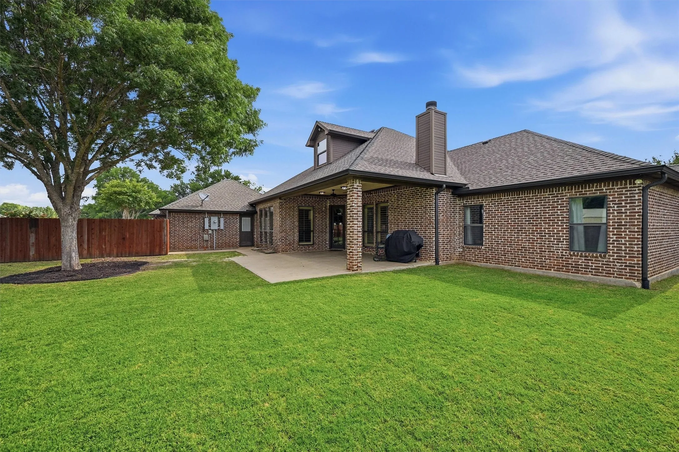 Expansive rear yard featuring a large concrete patio, substantial brick exterior, and a dormer window