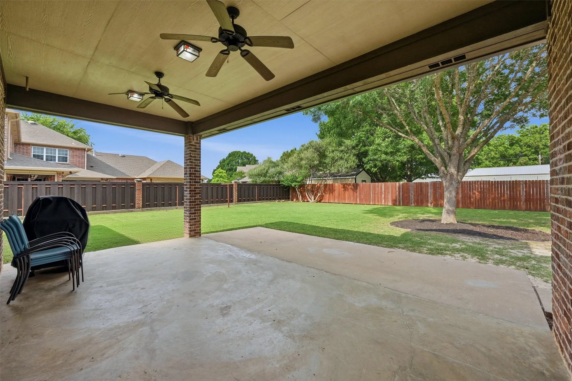 Covered patio with a concrete surface and brick columns, featuring two ceiling fans with integrated lighting