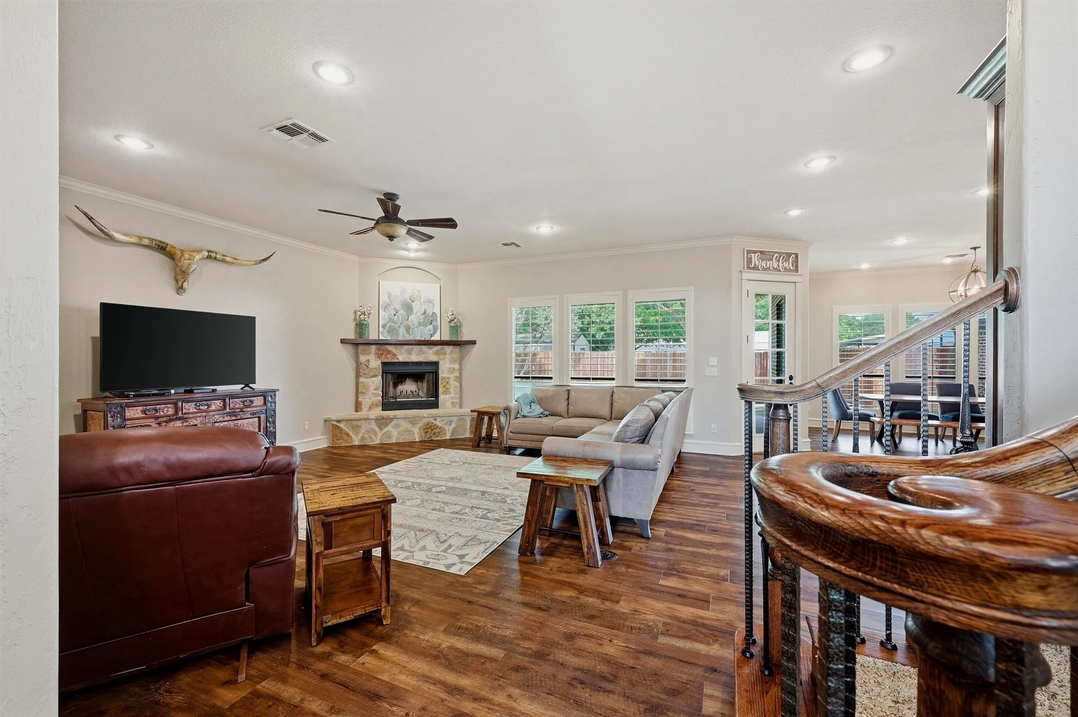 Open-concept living space featuring wood-finish flooring, a stone-surround fireplace, recessed lighting, and a ceiling fan
