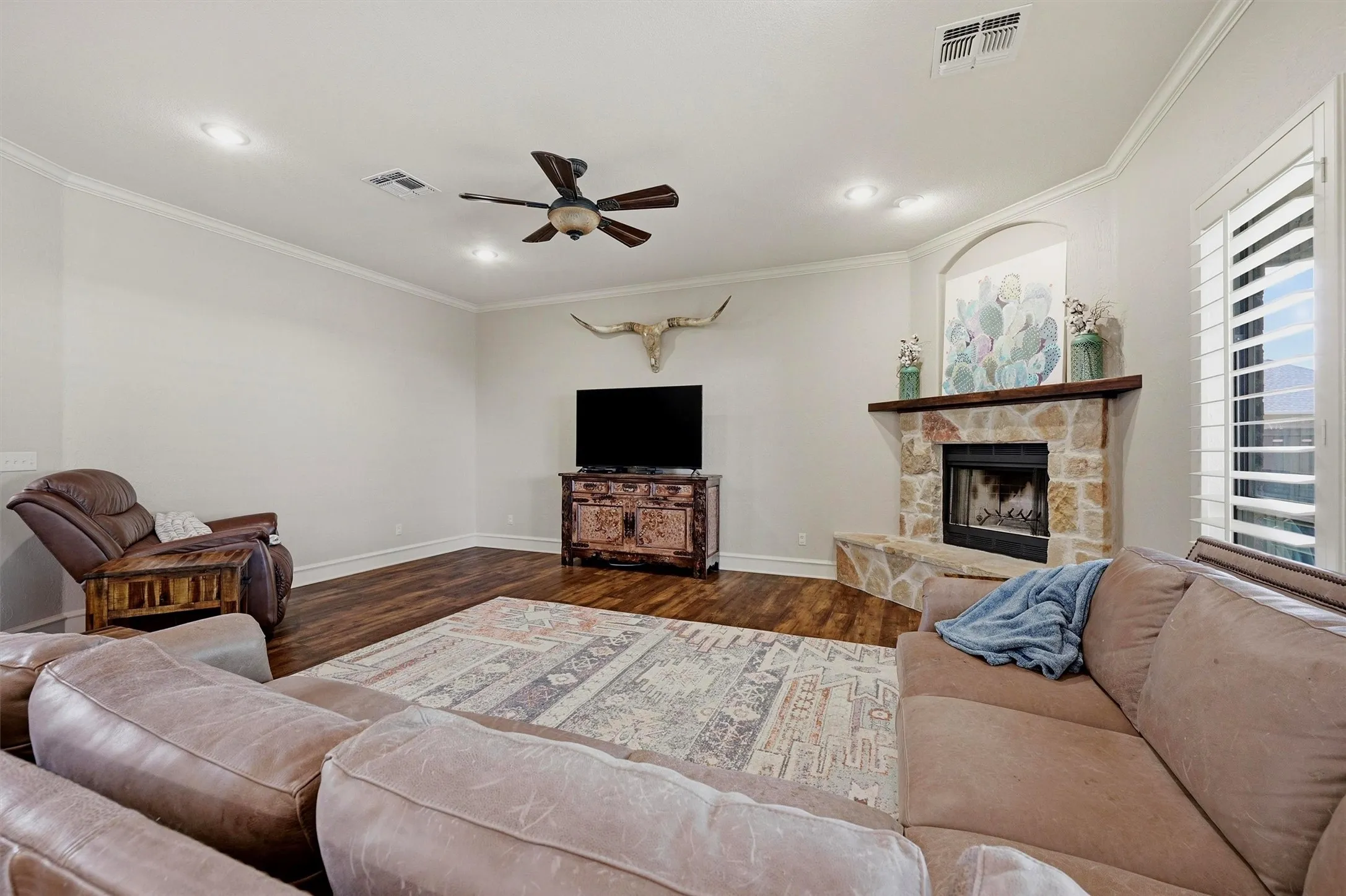 Living space featuring a stone fireplace with a wood-beam mantel, wood-finish flooring, and crown molding